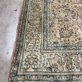 Tabriz-style rug corner, cream with teal-blue border and dense floral designs.