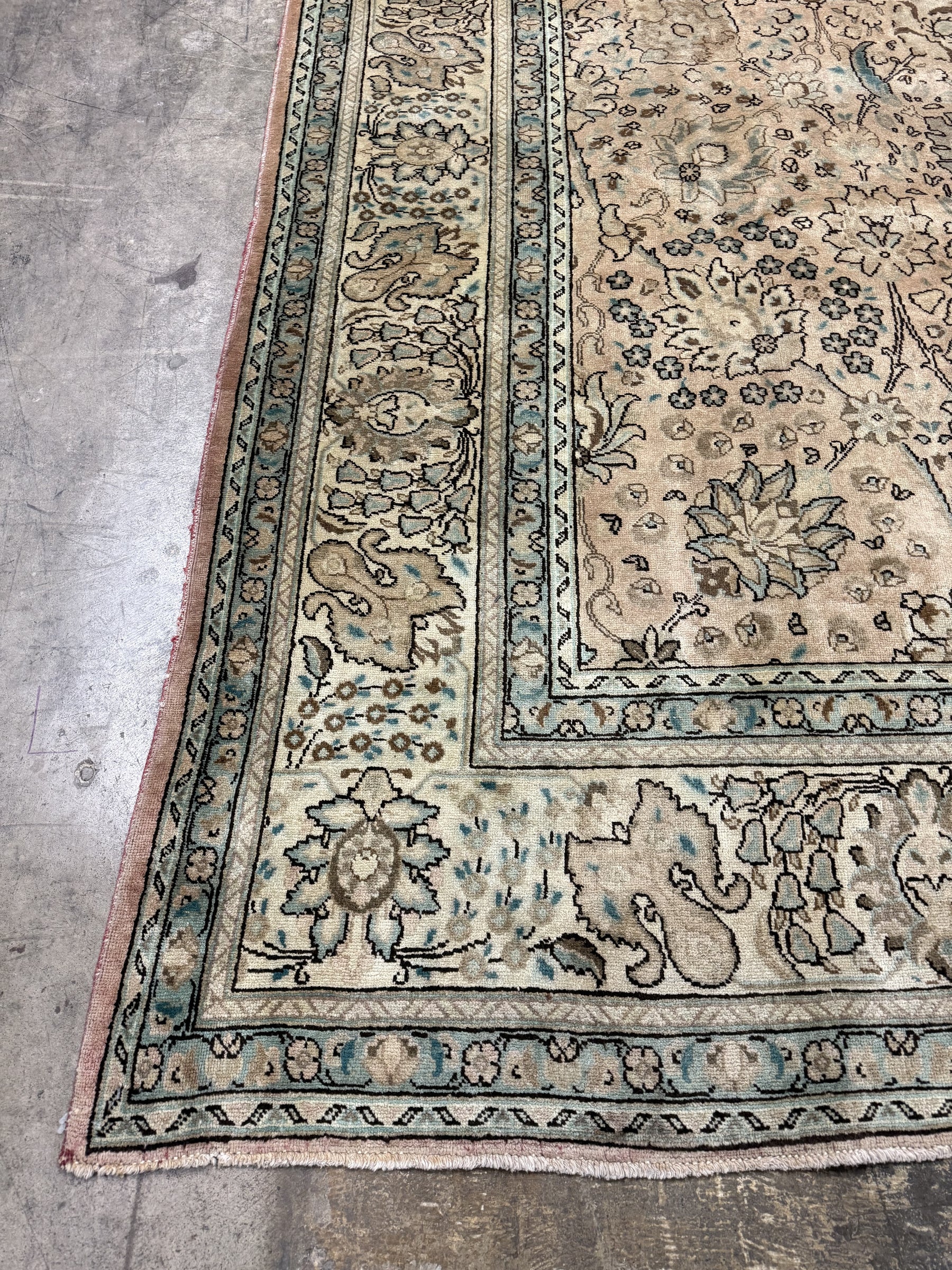Tabriz-style rug corner, cream with teal-blue border and dense floral designs.