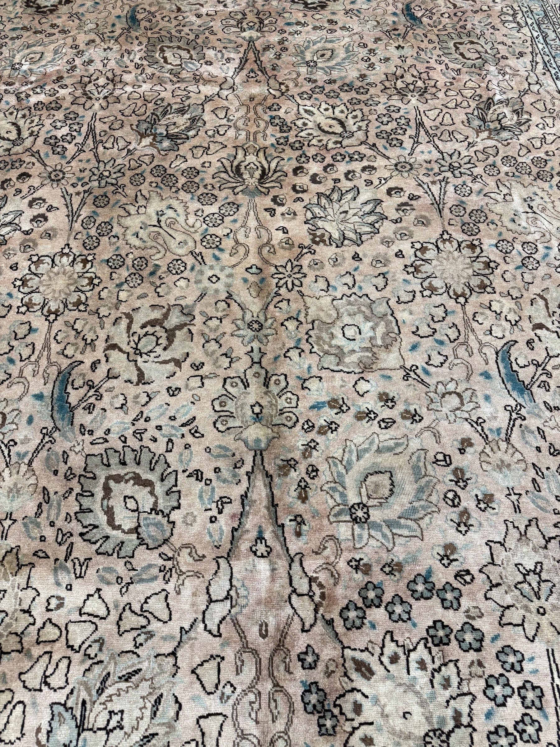 Close-up of Tabriz-style rug pile: cream background with teal-blue vine and flower motifs.
