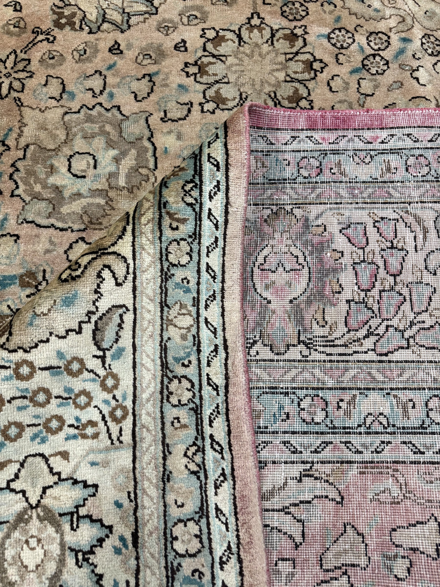 Tabriz-style rug corner close-up with teal-blue border and pink backing at edge.