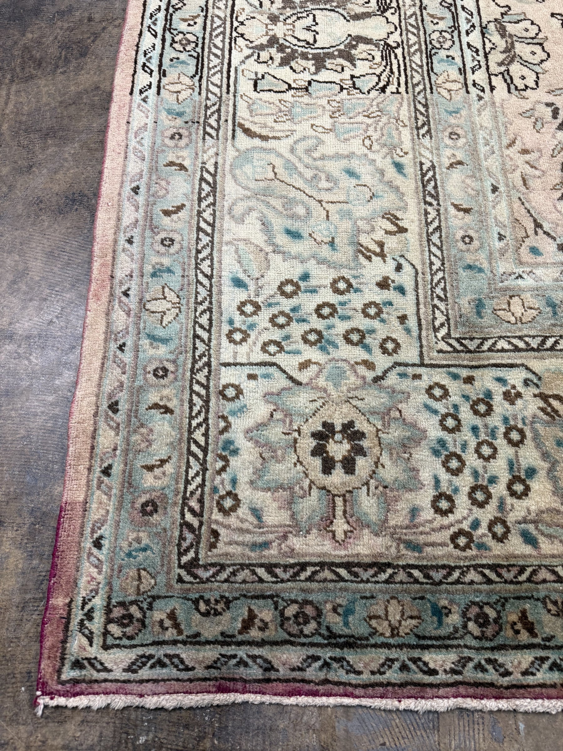 Cream rug corner with teal vine border, floral motifs, and red-framed edge