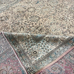 Cream rug with teal border, central floral design, and red-trimmed edges
