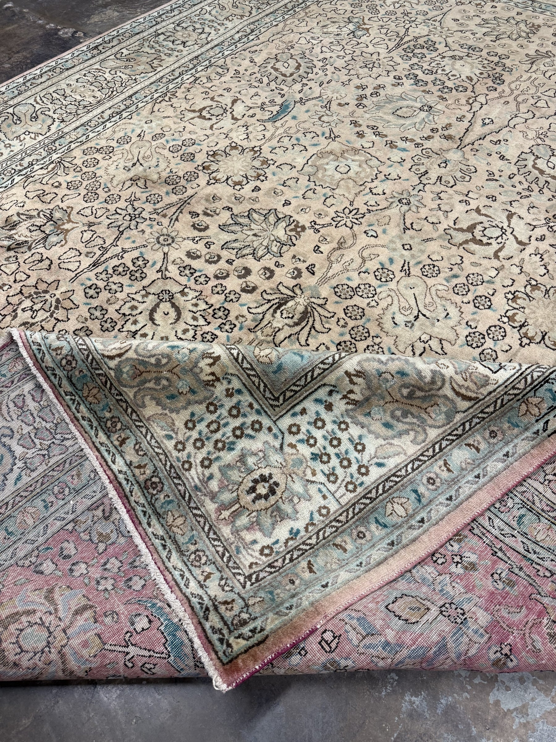 Cream rug with teal border, central floral design, and red-trimmed edges
