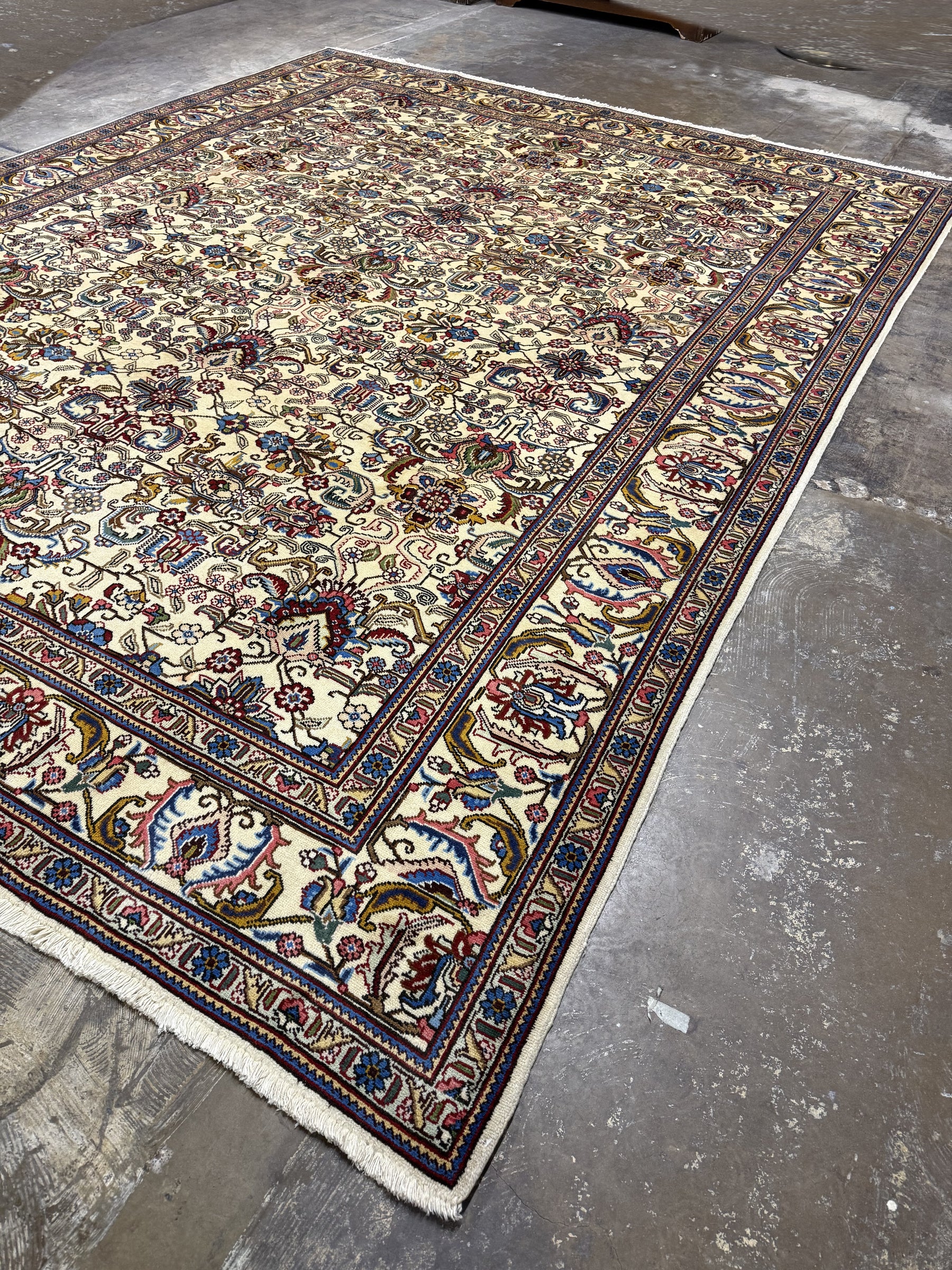 Tabriz rug corner with red and blue floral motifs, dark navy border stripe, fringe