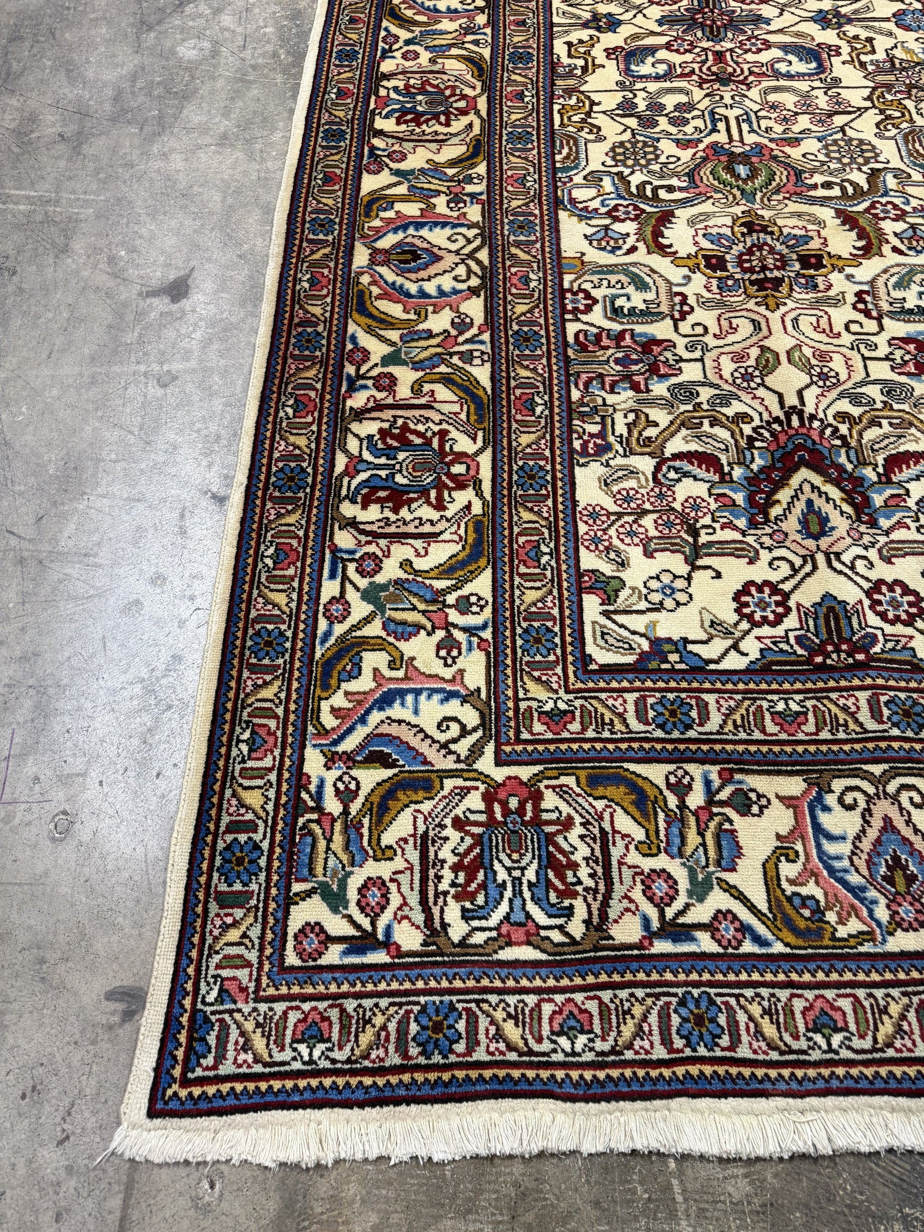 Tabriz rug border detail with rosette and scrolling motifs in red, blue, gold on cream