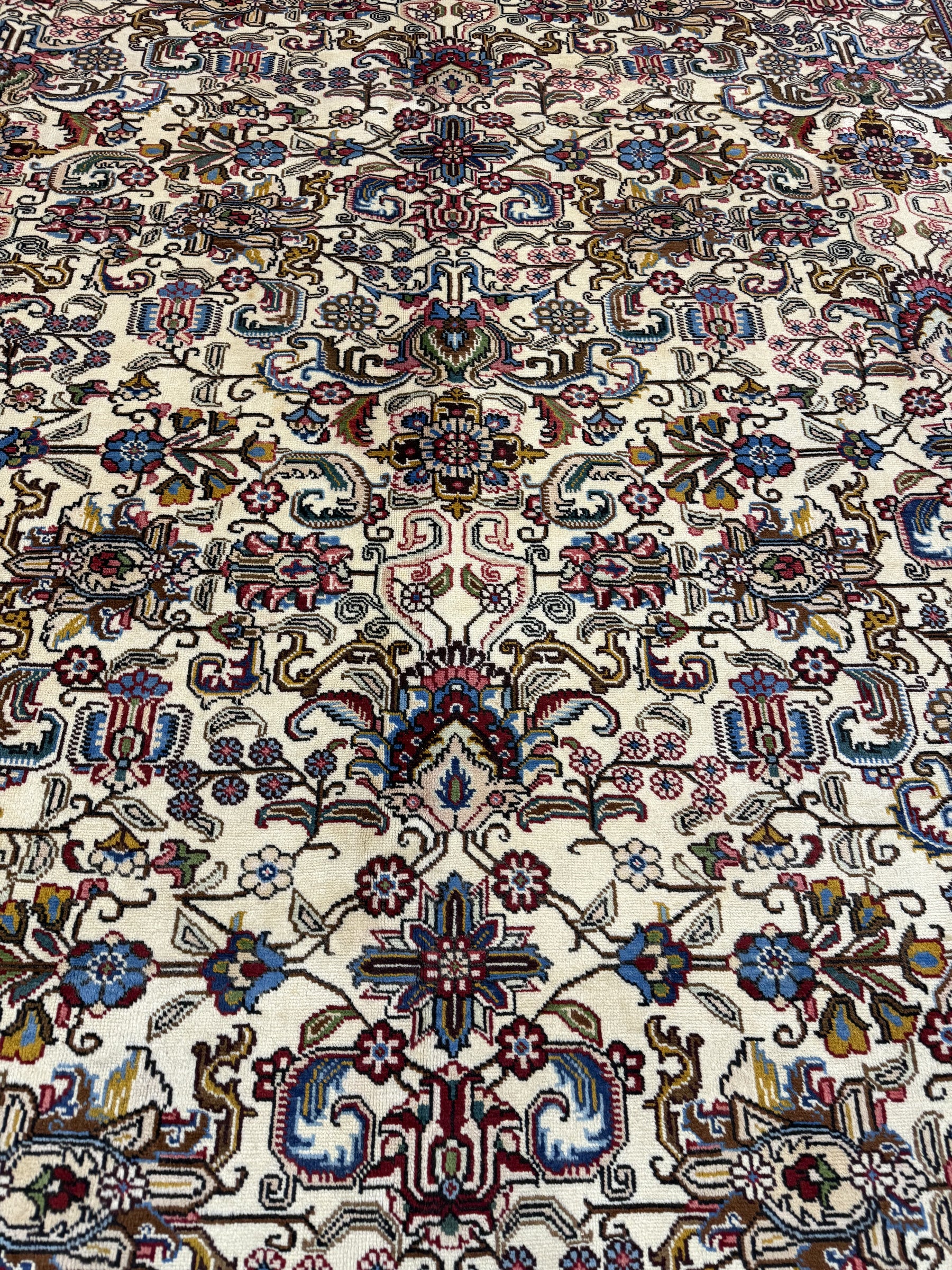 Tabriz rug close-up: cream background with red, blue, green floral scrollwork