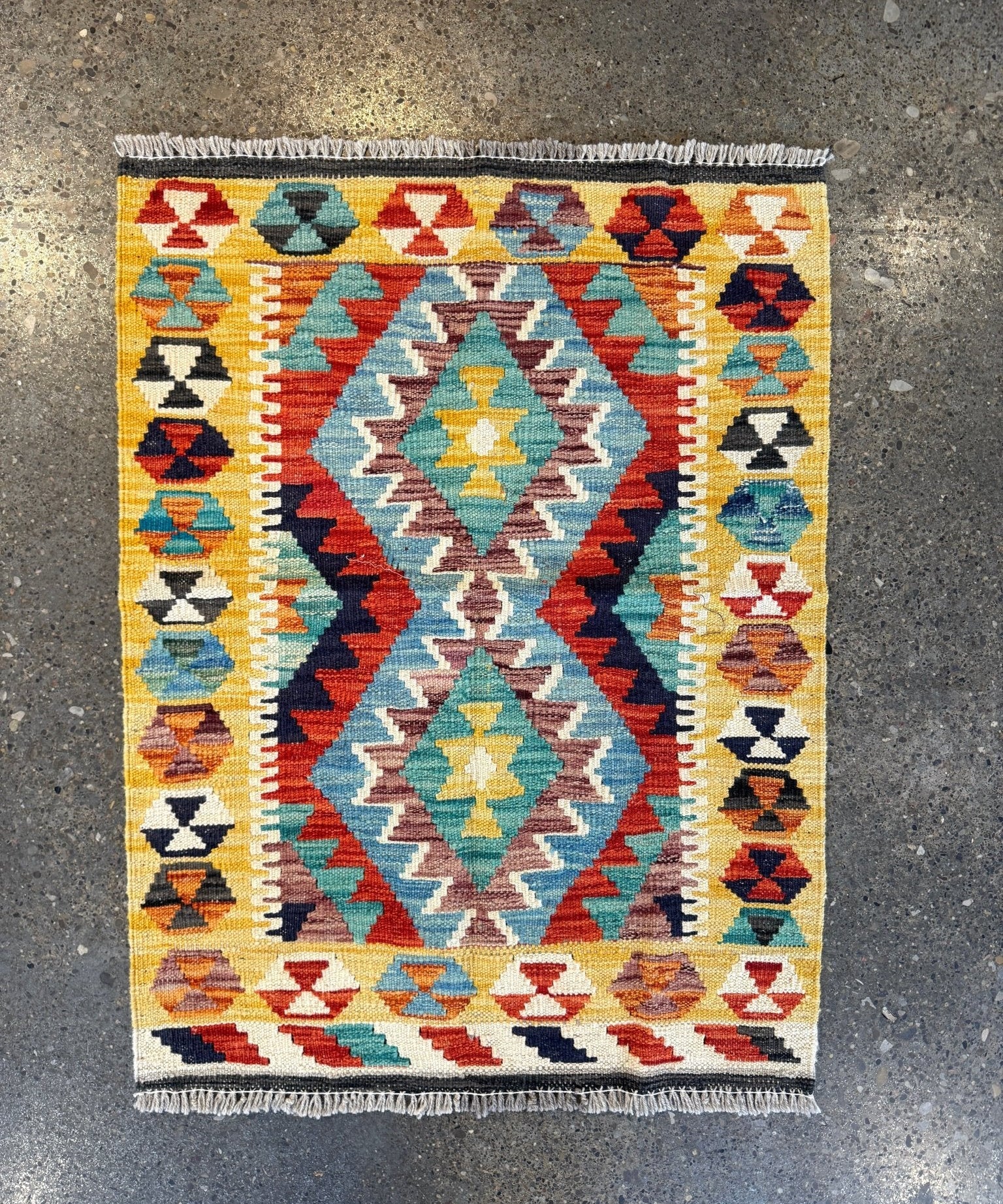Kilim rug with diamond medallions in yellow, teal, red, navy, and cream; fringe edge