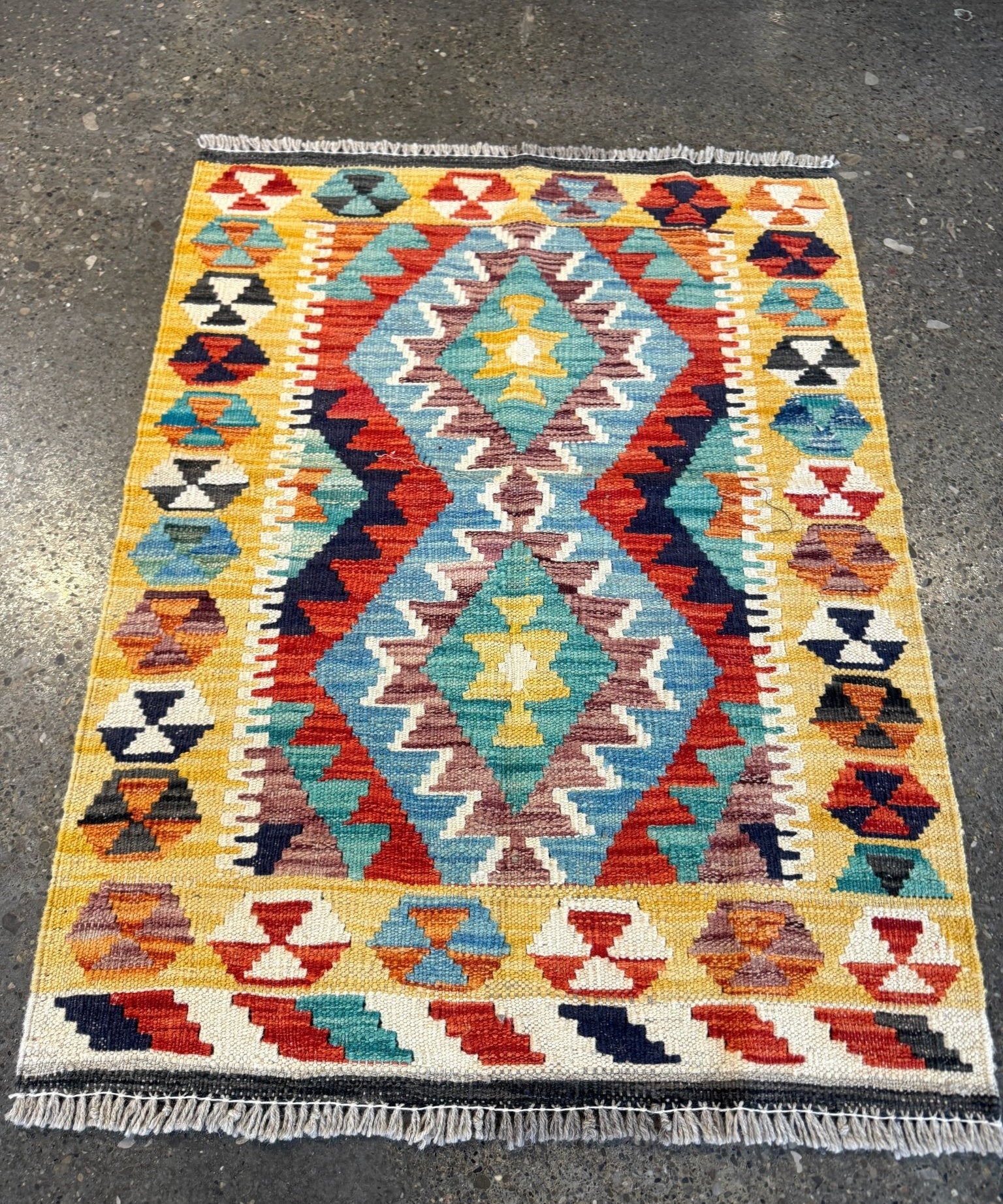 Kilim rug with geometric diamonds and zigzags in yellow, teal, red, and navy; short fringe