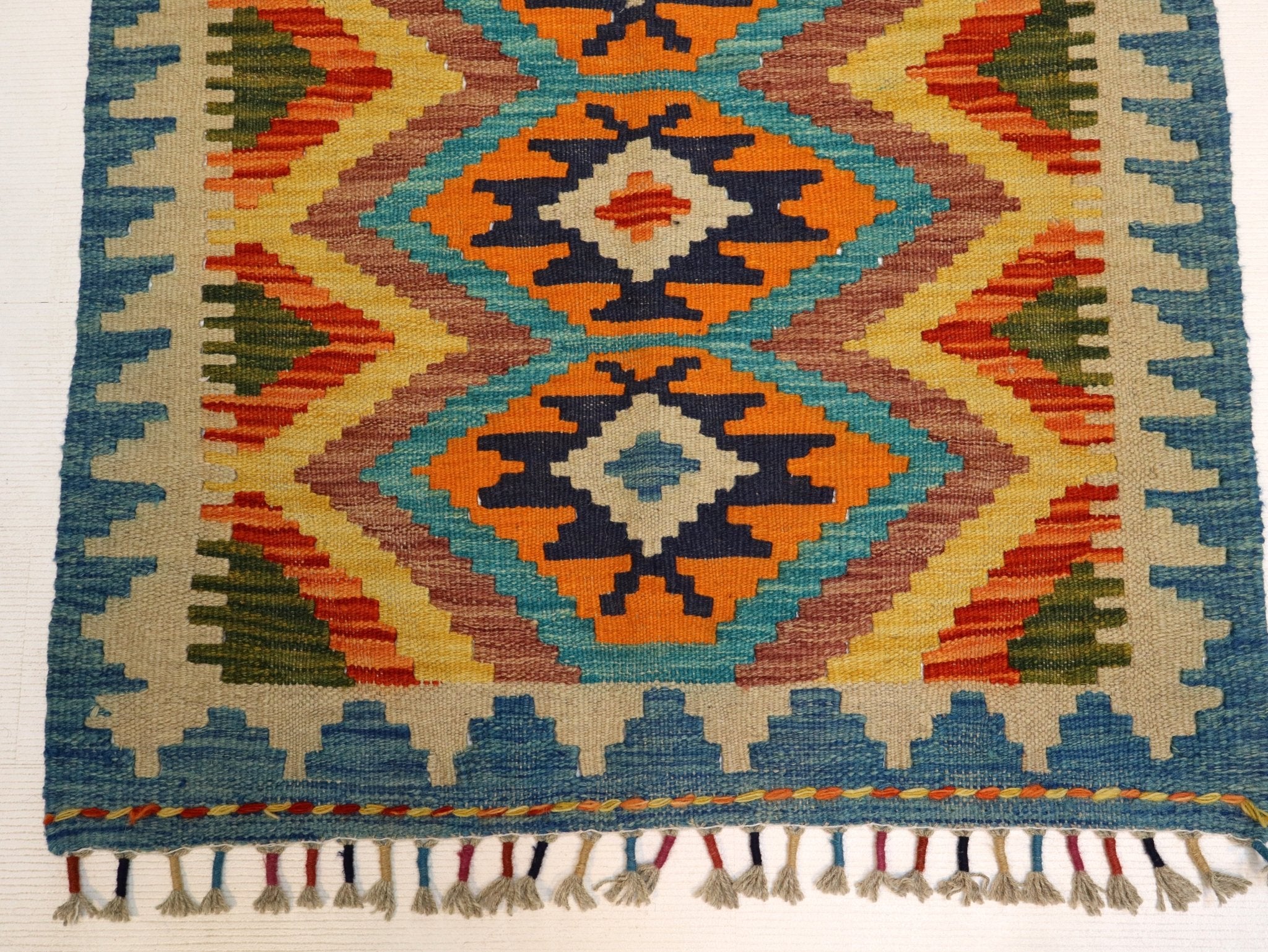 Kilim rug border with patterned band in orange, teal and navy and long tassels