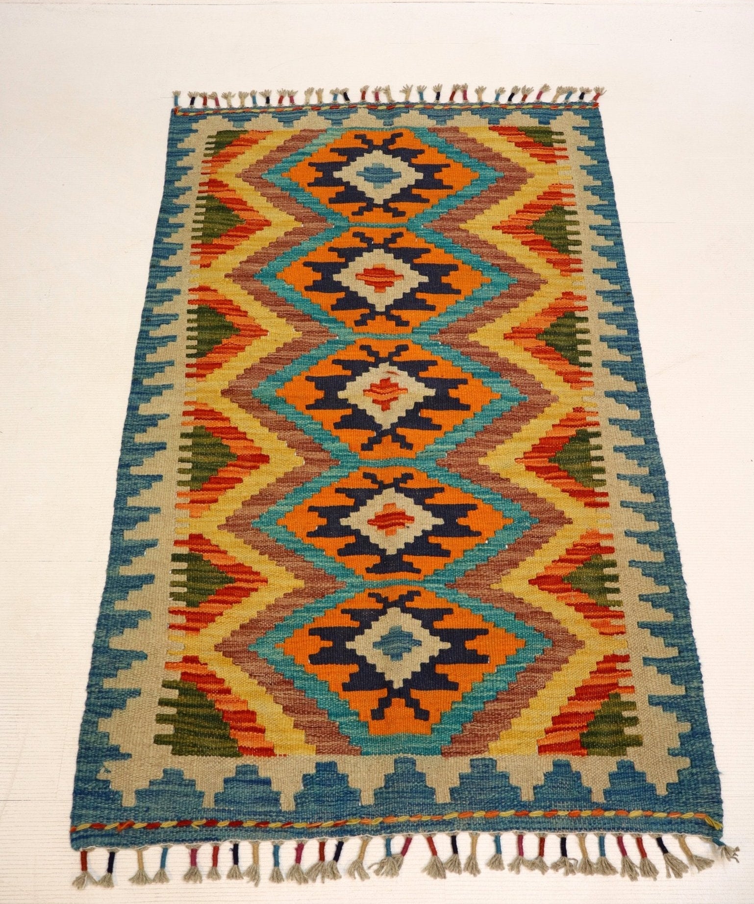 Geometric kilim rug with teal field, orange zigzags, navy accents and fringe