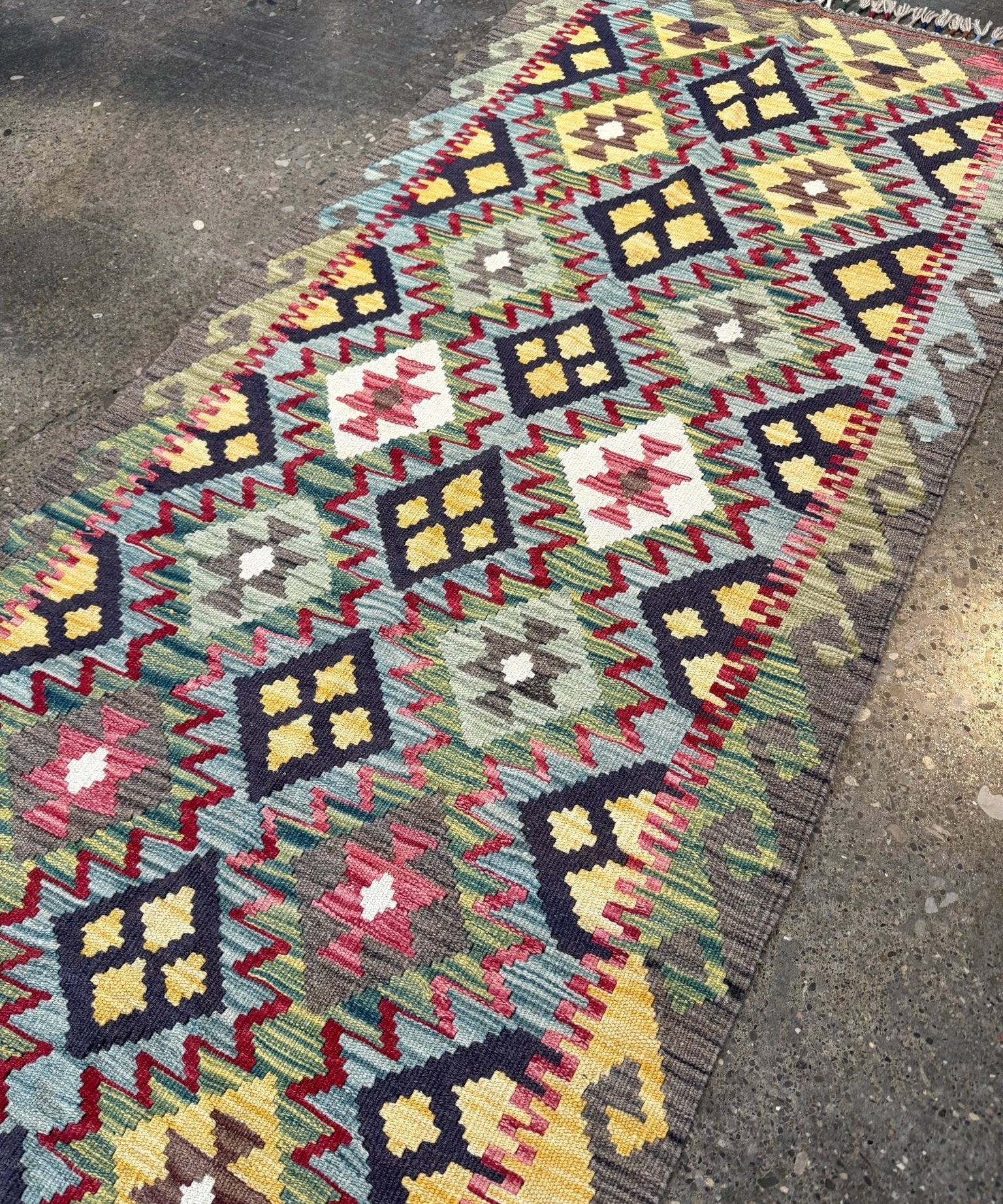 Wide view of multicolor kilim rug with zigzag diamonds and small medallion shapes; fringed edge