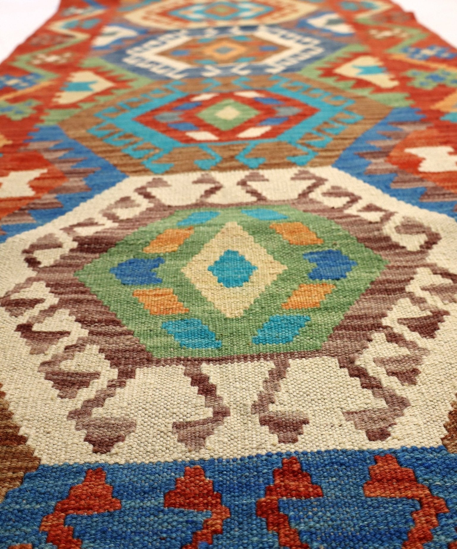 Close-up of kilim rug medallion with blue, orange, green, and beige geometric patterns.