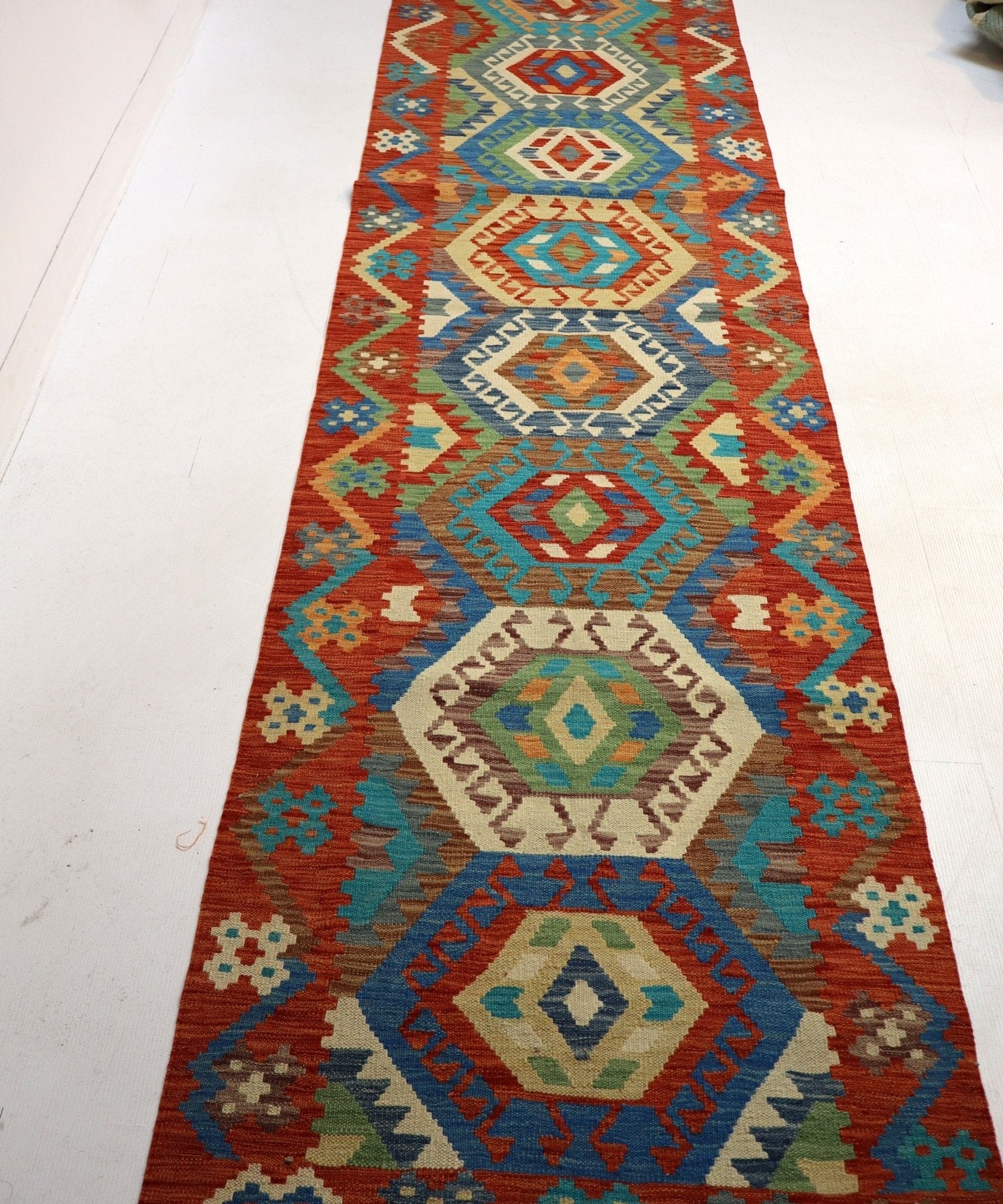 Long kilim rug with stacked diamond medallions, multicolor geometric field, fringed end.