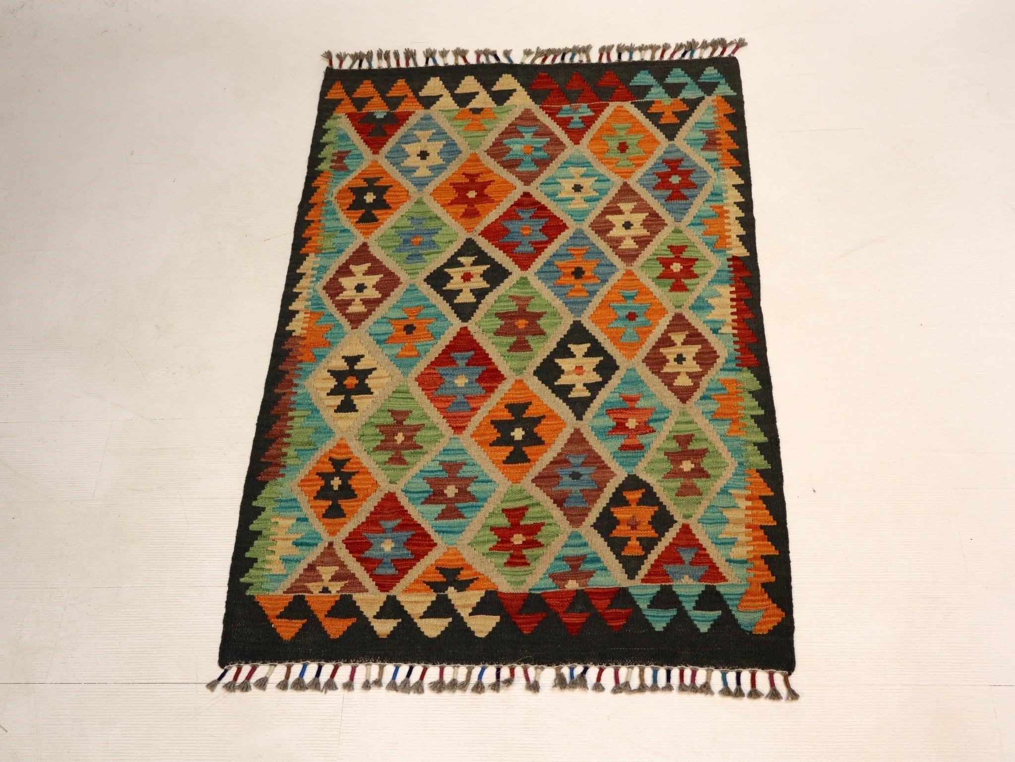 Full view of geometric kilim rug with multicolor diamond pattern and fringe edging