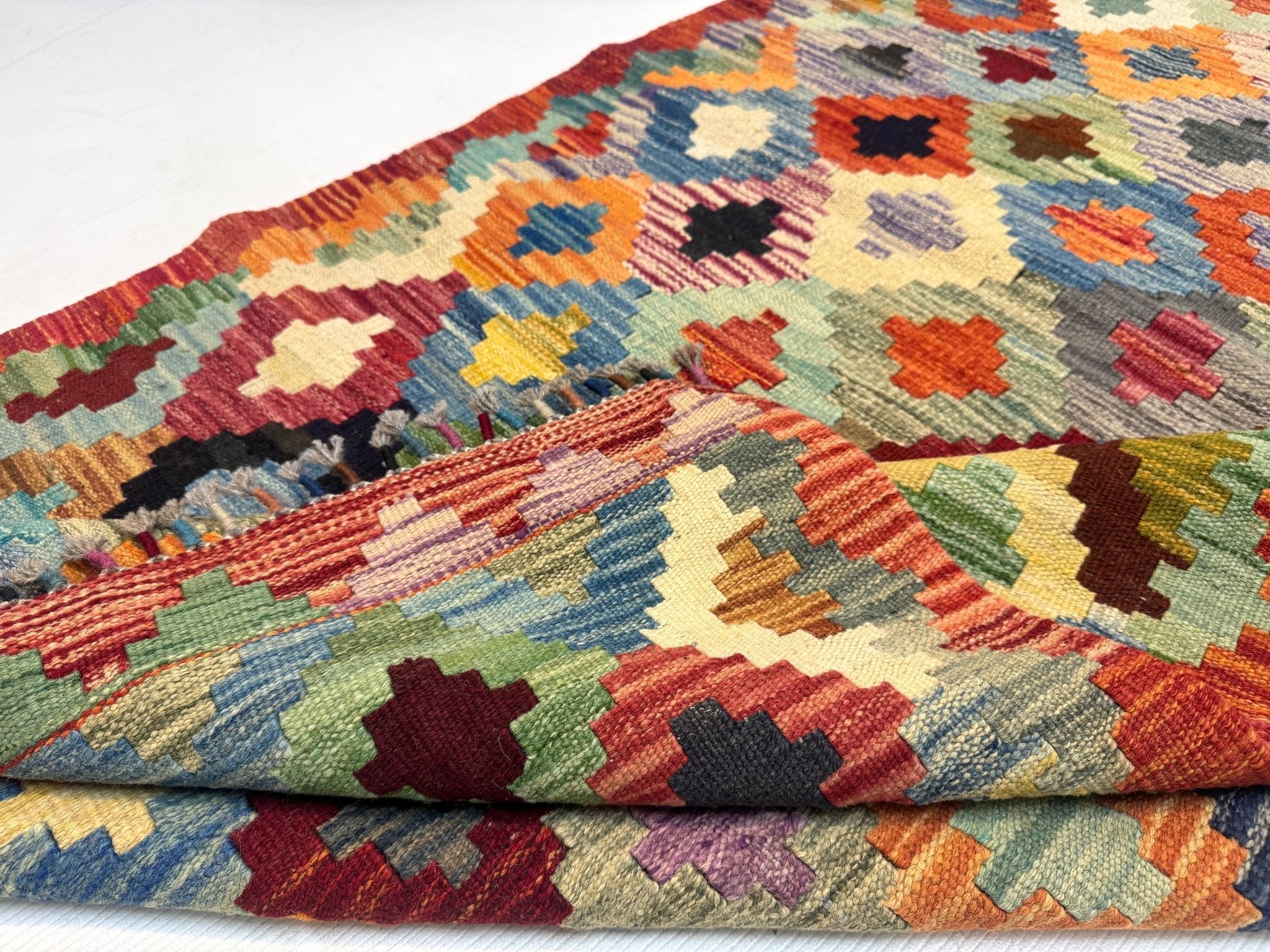 Kilim rug corner with multicolor cross-and-diamond pattern and braided fringe edge