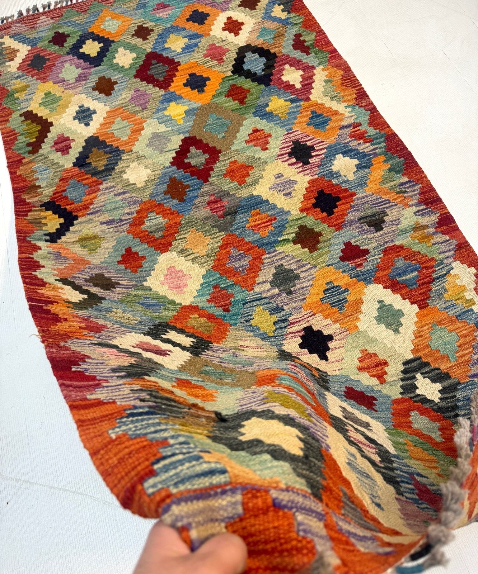 Afghan kilim rug with cream ground, orange accents, multicolor geometric motifs and fringes