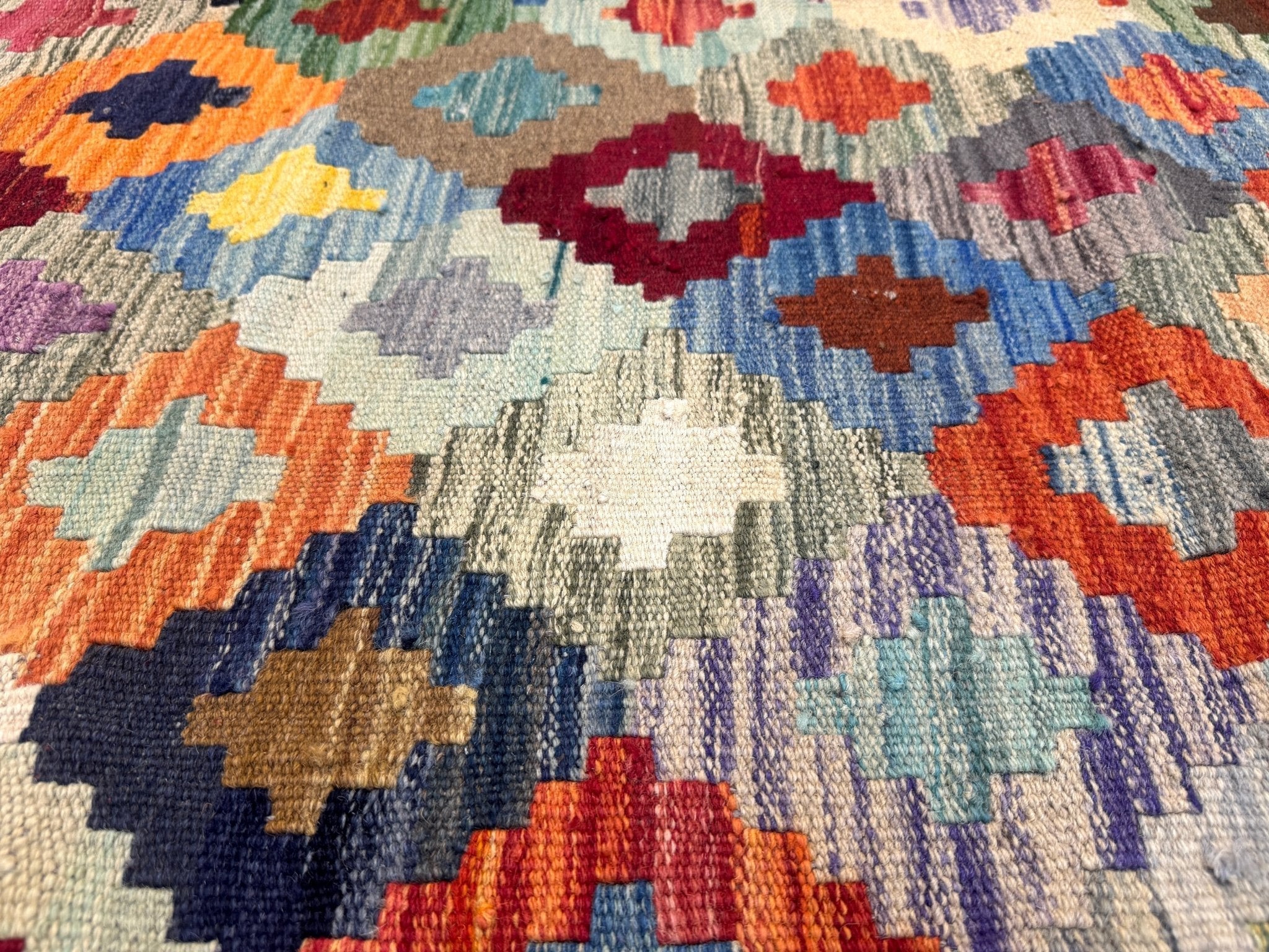 Kilim rug close-up with light gray background and blue, orange, purple and cream motifs