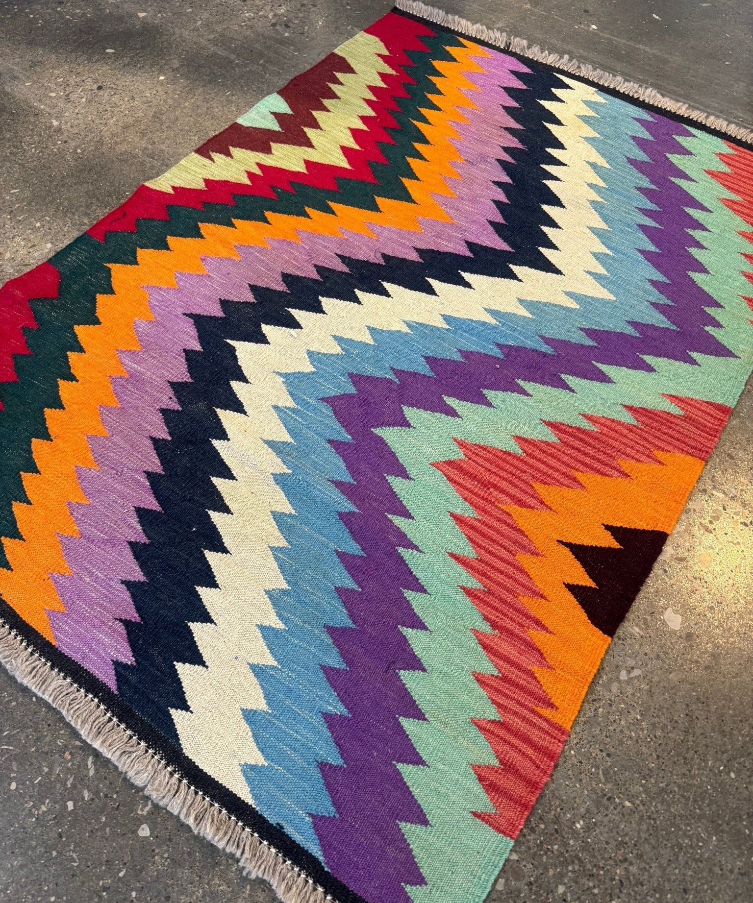 Vibrant multicolor kilim rug with zigzag chevrons and fringed border along one edge.