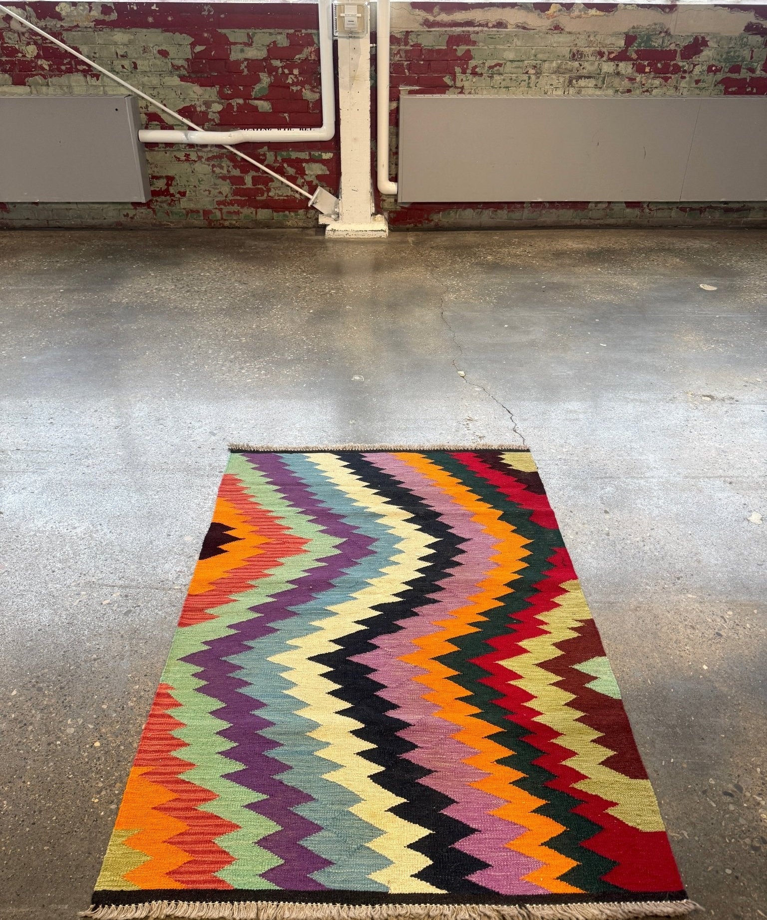 Multicolor kilim rug with zigzag chevrons and short fringed edges, on the floor.