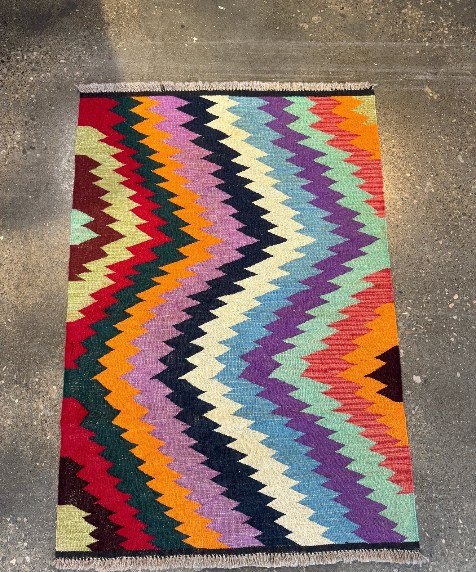 Multicolor kilim rug with zigzag chevrons on red, purple, teal, and cream ground