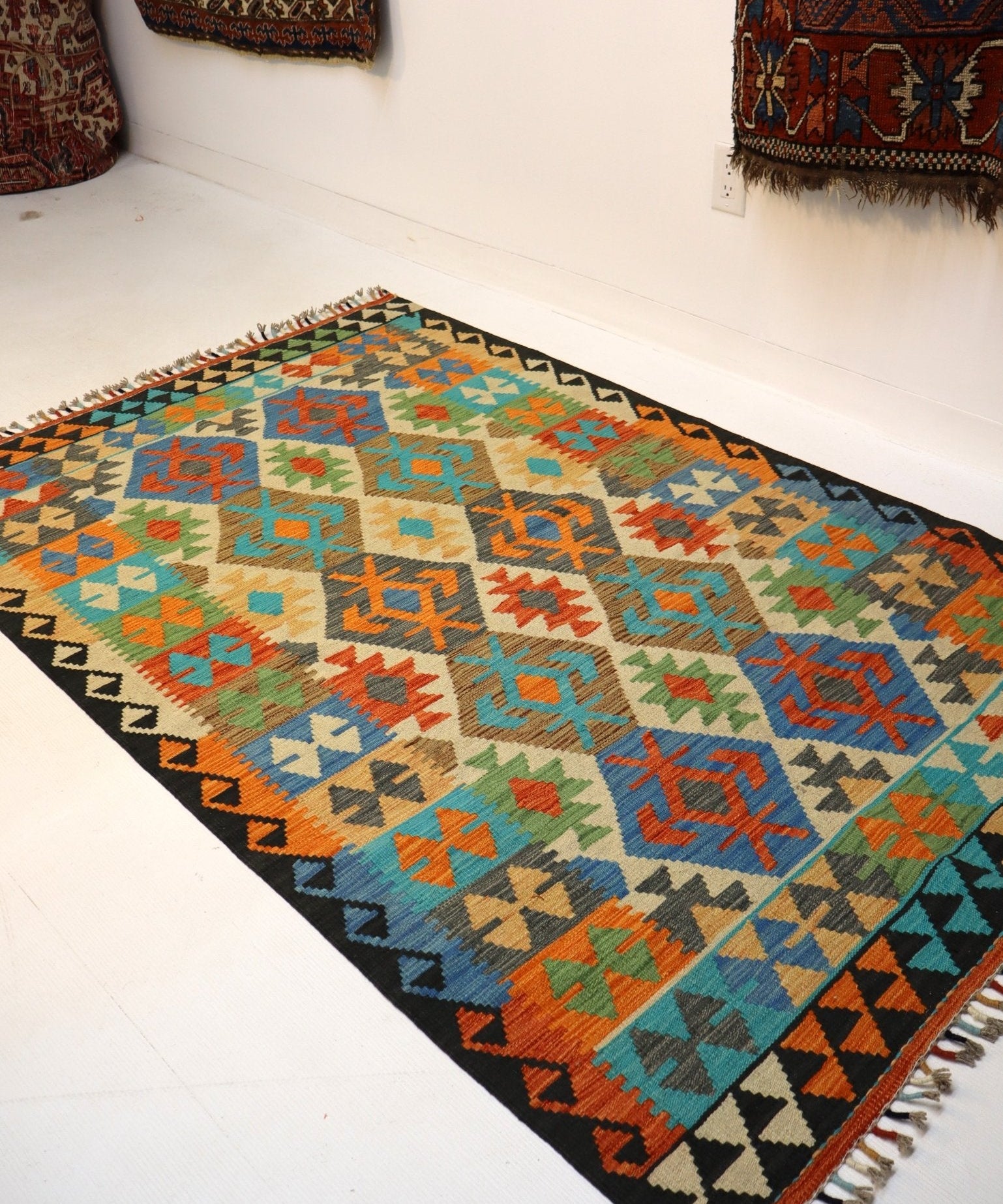 Geometric Afghan-style kilim rug with multicolor diamond motifs and fringed edge on floor