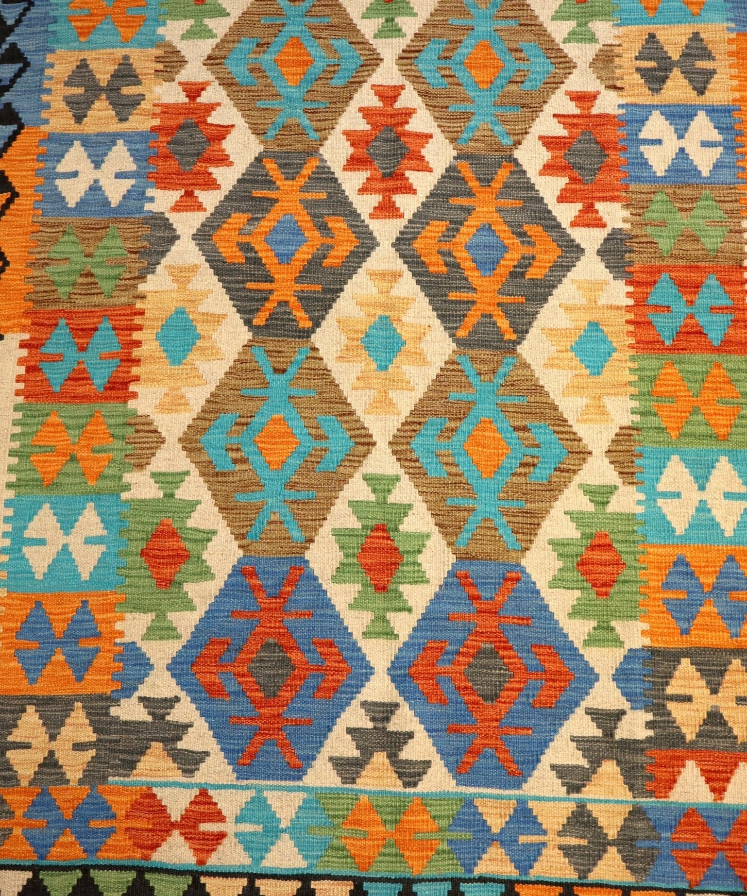 Kilim rug section with repeating diamond and arrow shapes in blue, orange, teal, green, and cream