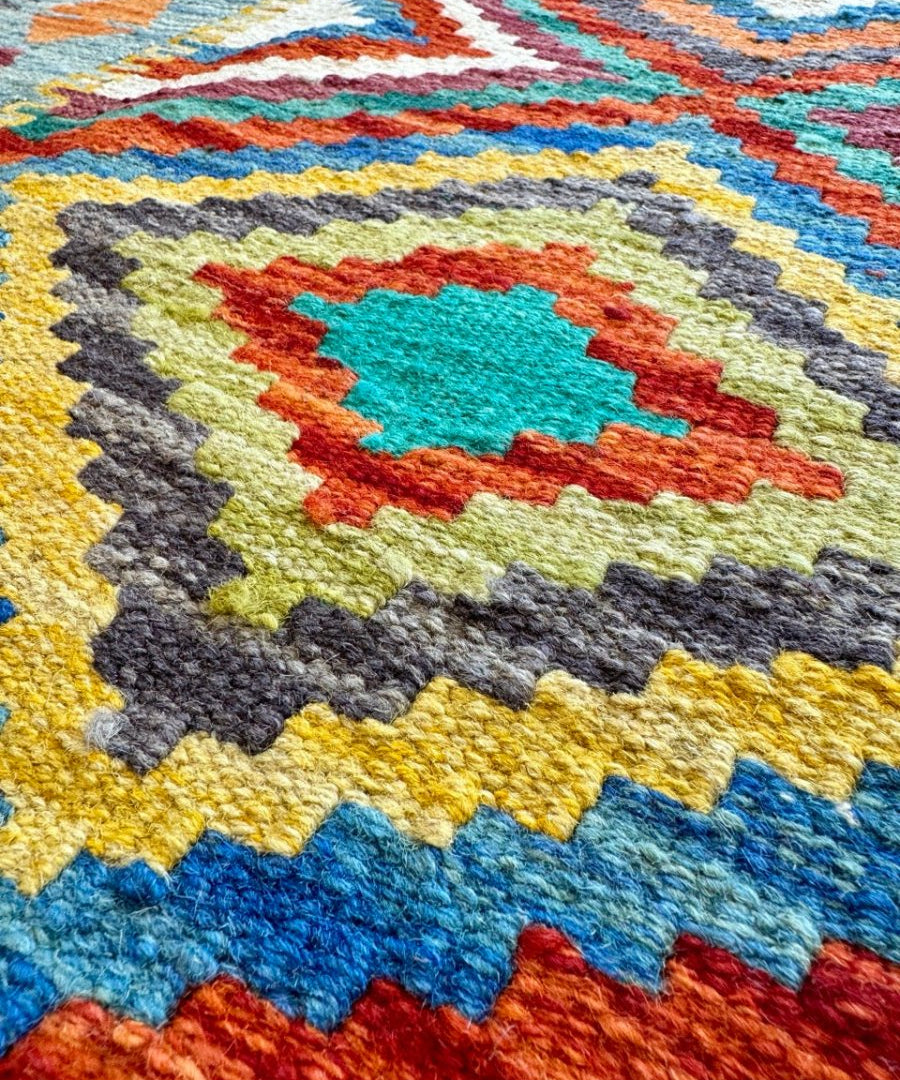 Colorful kilim rug with a central diamond motif and zigzag border, fringed edge