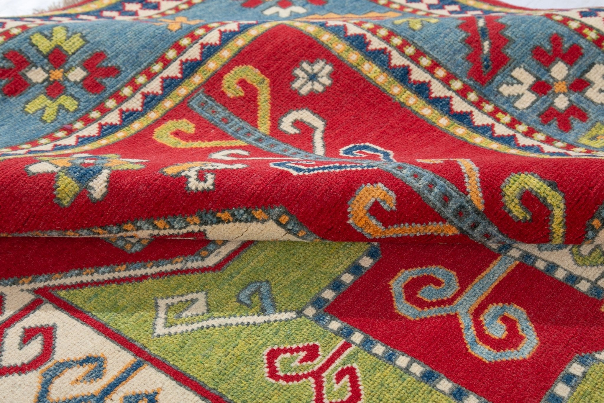 Folded edge and wool pile of red & green Kazak-inspired wool rug 24948.