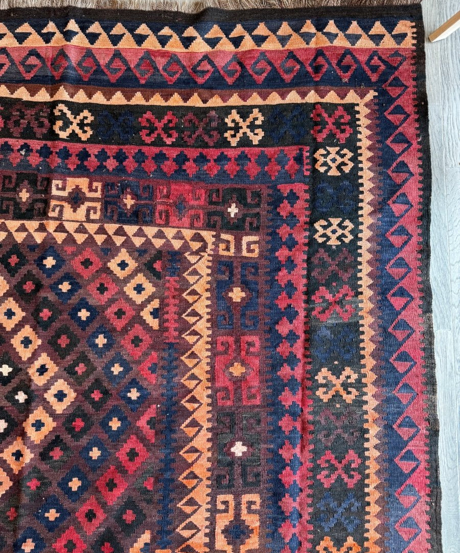 Close-up Afghan rug corner with navy, teal, pink, and cream geometric motifs and fringe