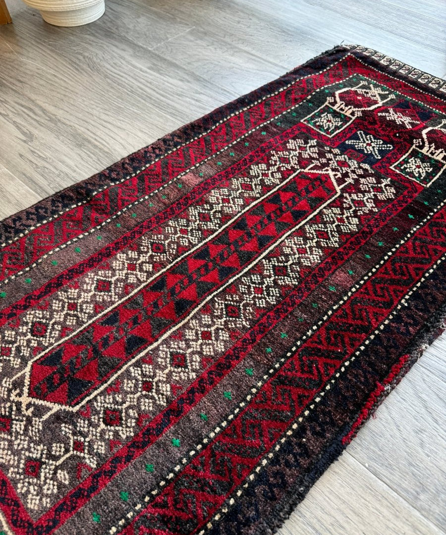 Antique saddlebag rug with red stripes, dark border, and repeating geometric motifs