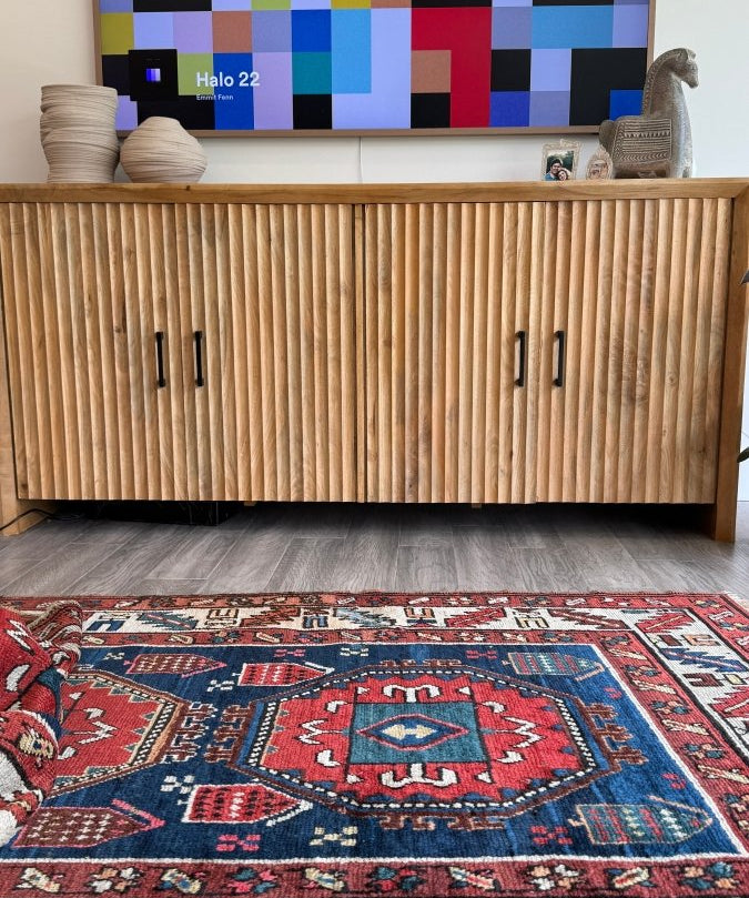 Kazak rug on floor with red and blue field and cream geometric border