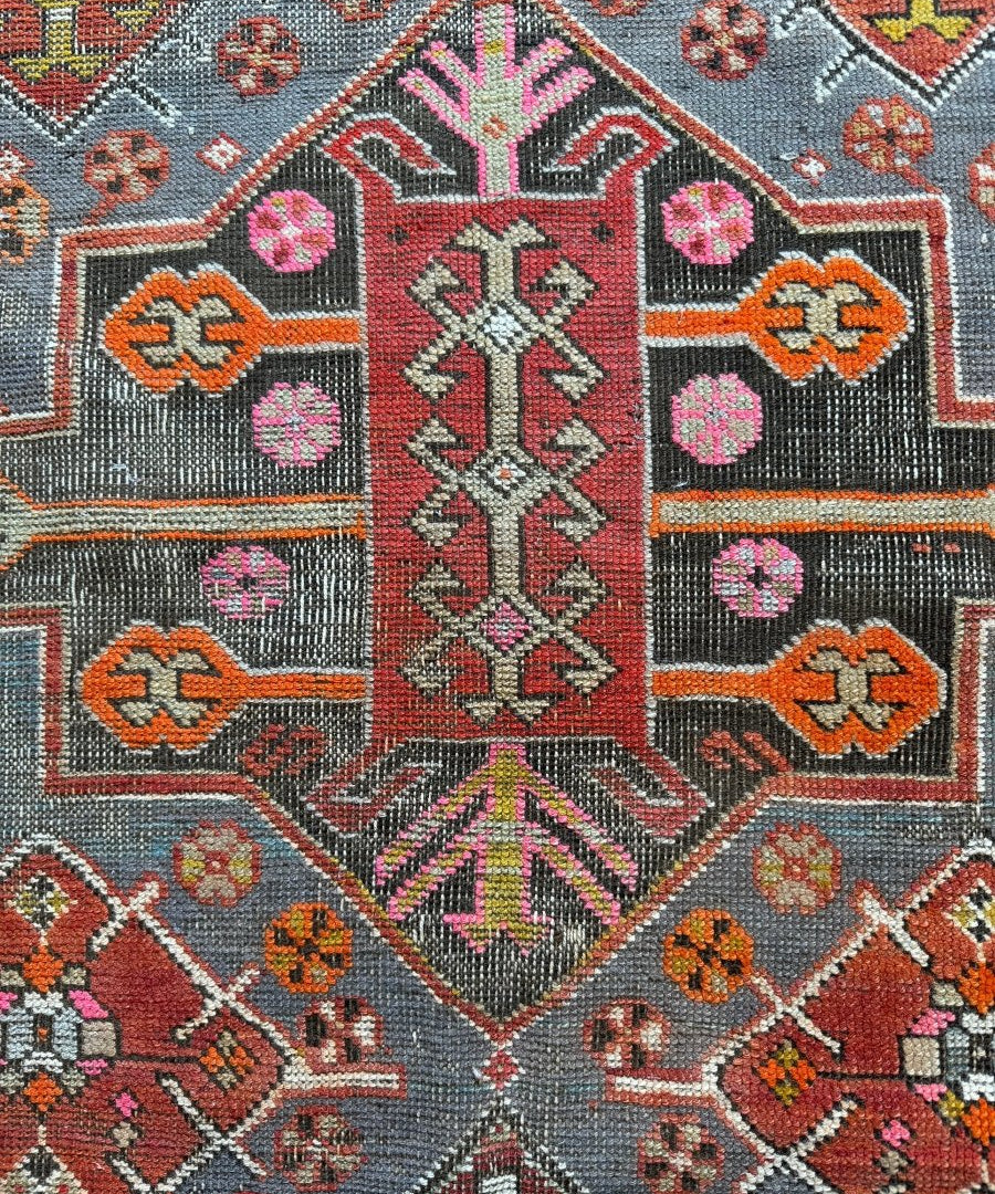 Antique Kazak rug close-up of central red medallion with pink, black, and white motifs