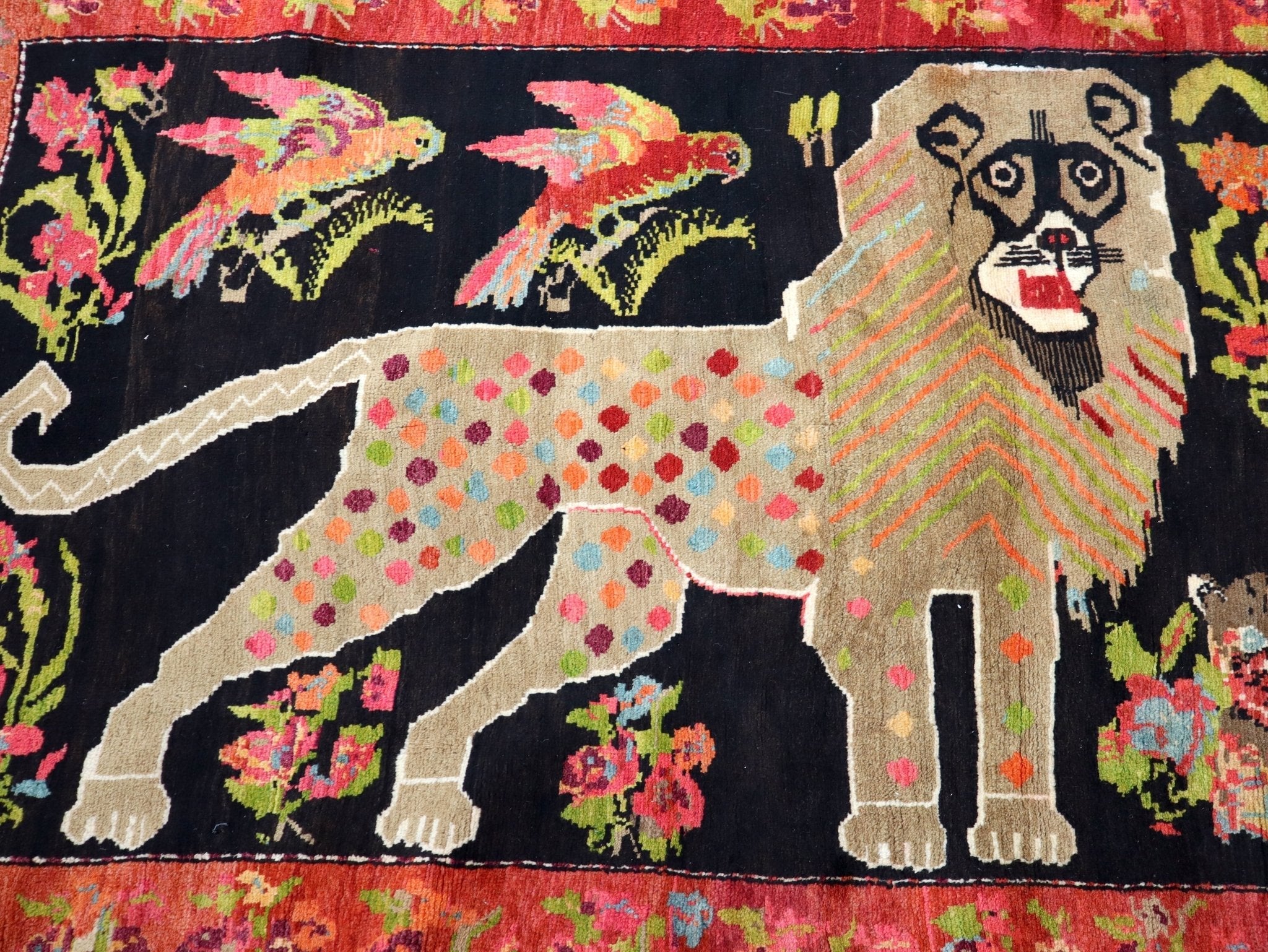 Close-up of patterned rug showing black field, beige animals, and pink-green flowers