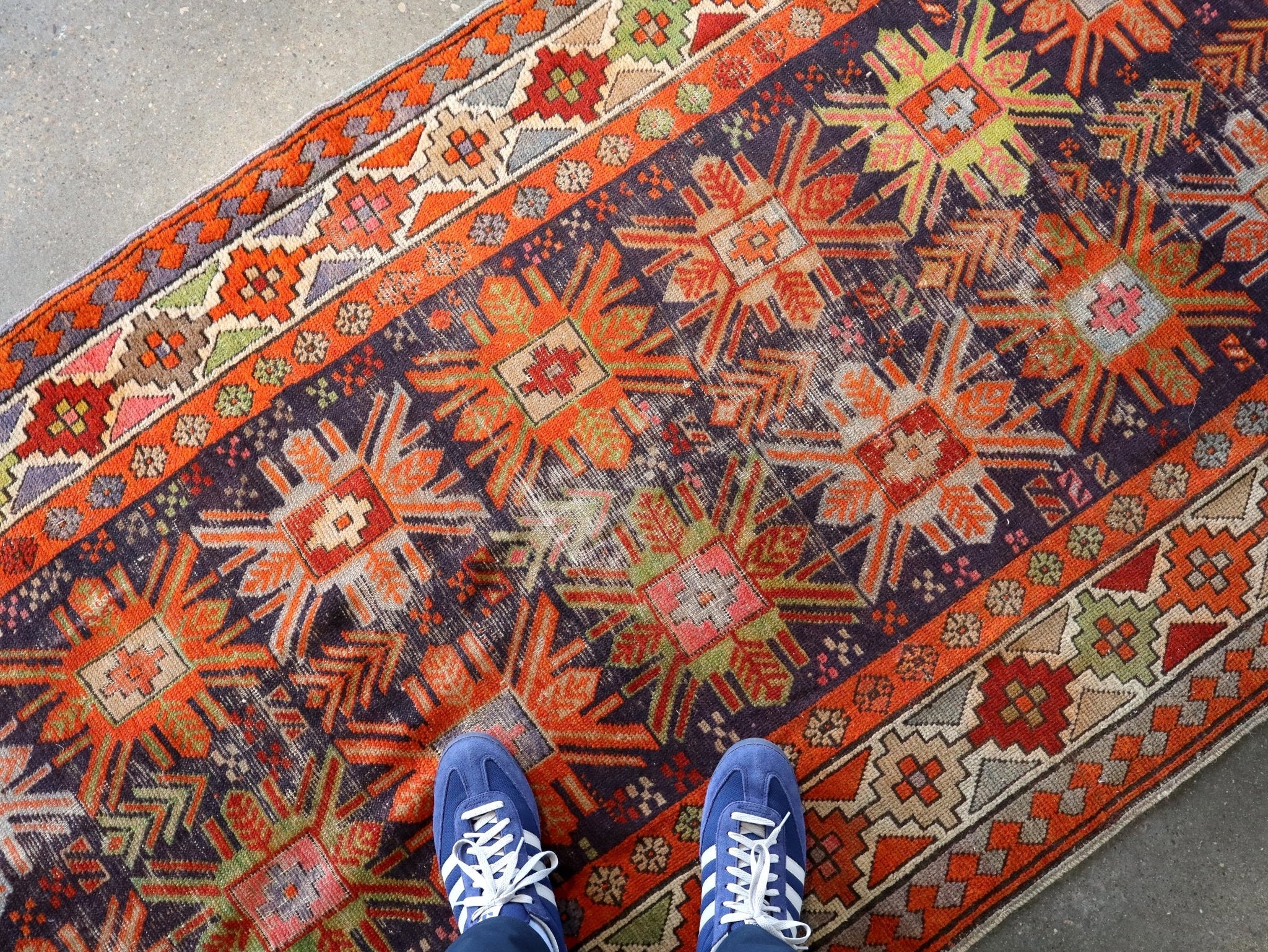 Orange and navy geometric rug with kilim motifs; two blue sneakers on top