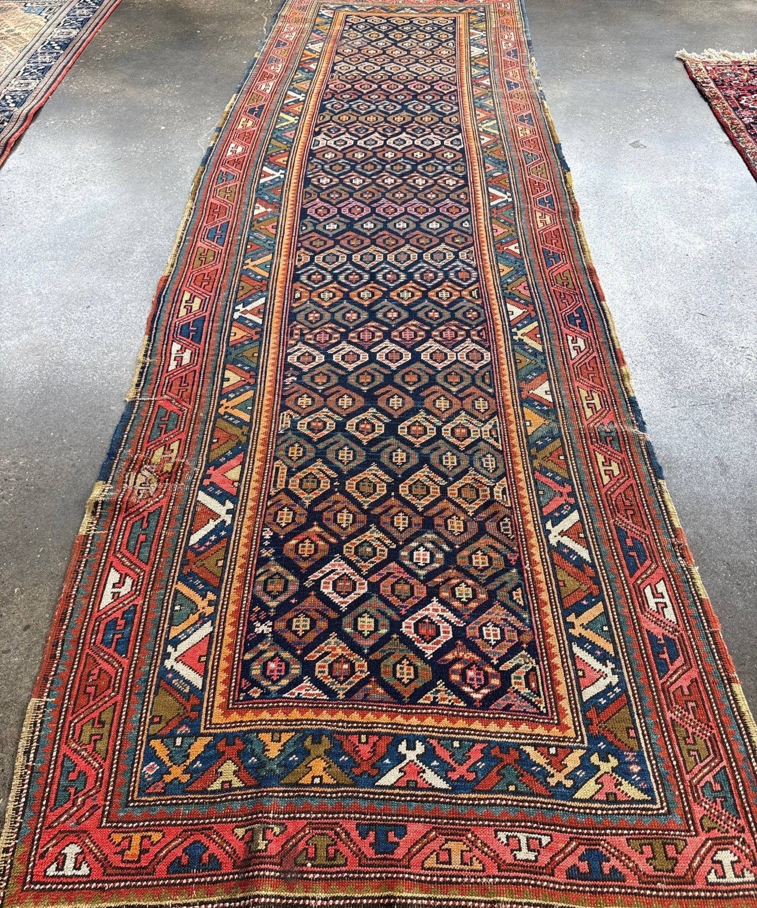 Kazak runner rug full view with dark blue center panel, red border, and repeating medallion motifs.