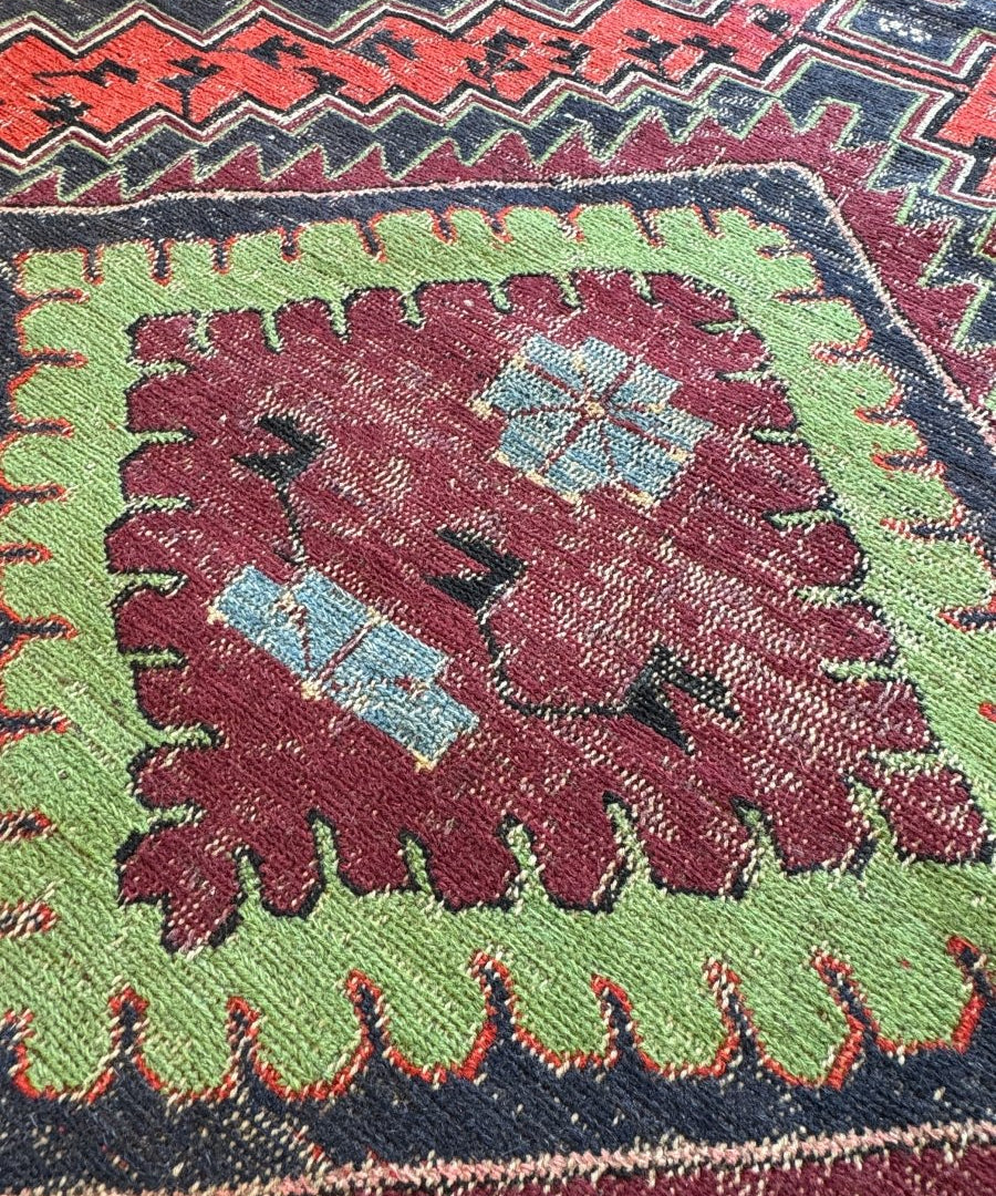 Soumak rug close-up with green ground, maroon floral motif, red border and fringed edge