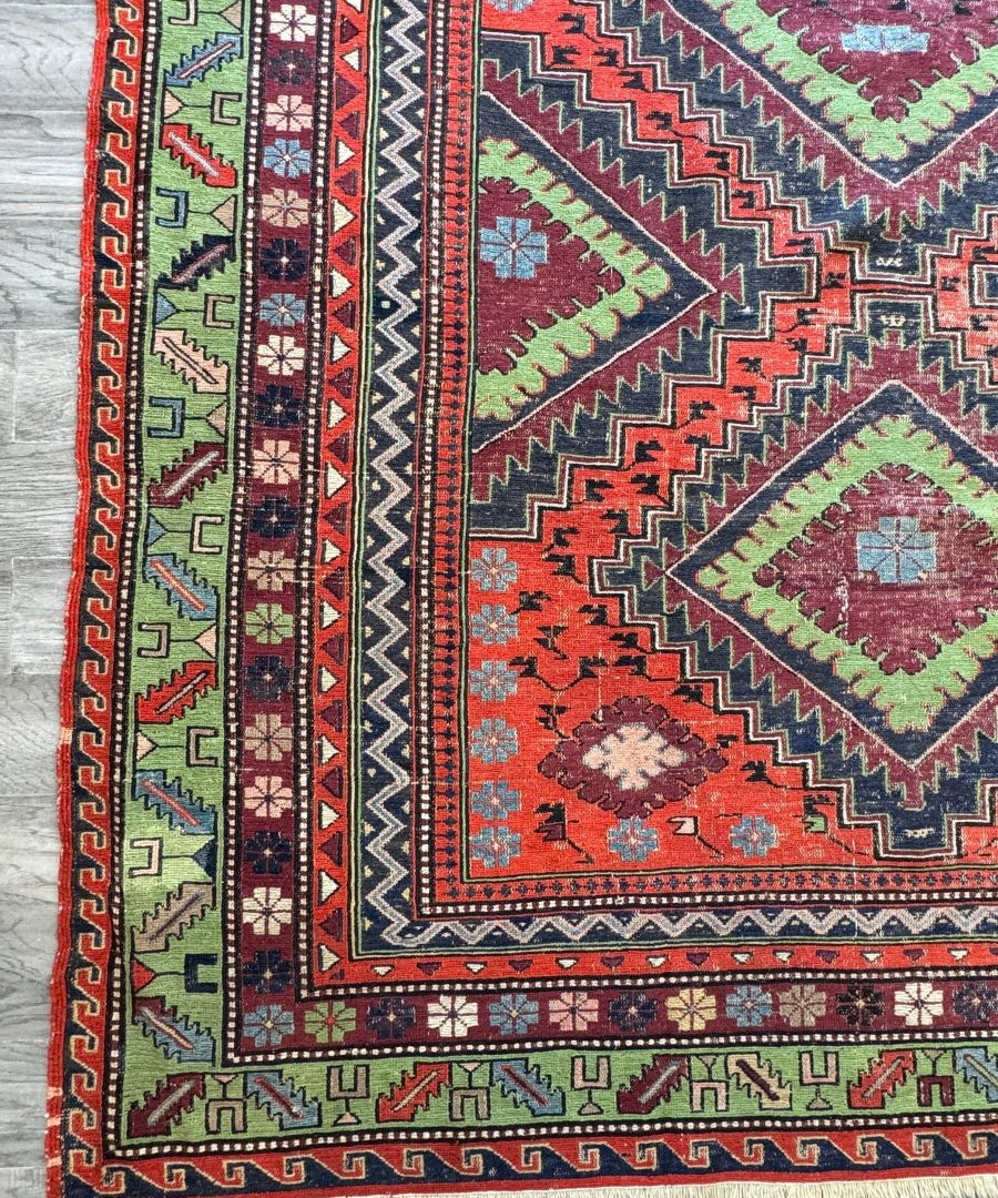 Soumak rug with dark border, red field, green accents, geometric medallions and fringe edges
