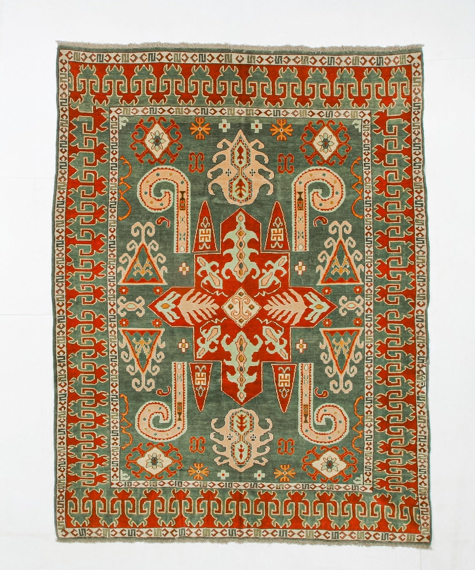 Kazak rug with dark green field, red medallions, and geometric border in cream and orange.