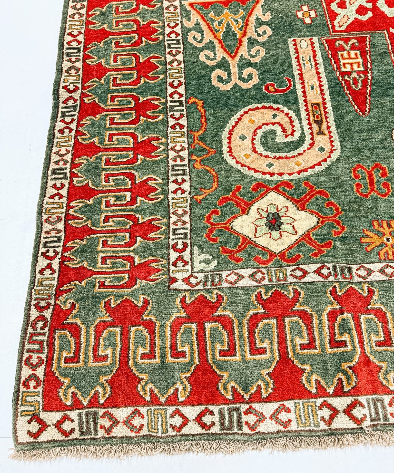 Kazak rug border close-up with repeating dark green and red geometric shapes, cream accents.