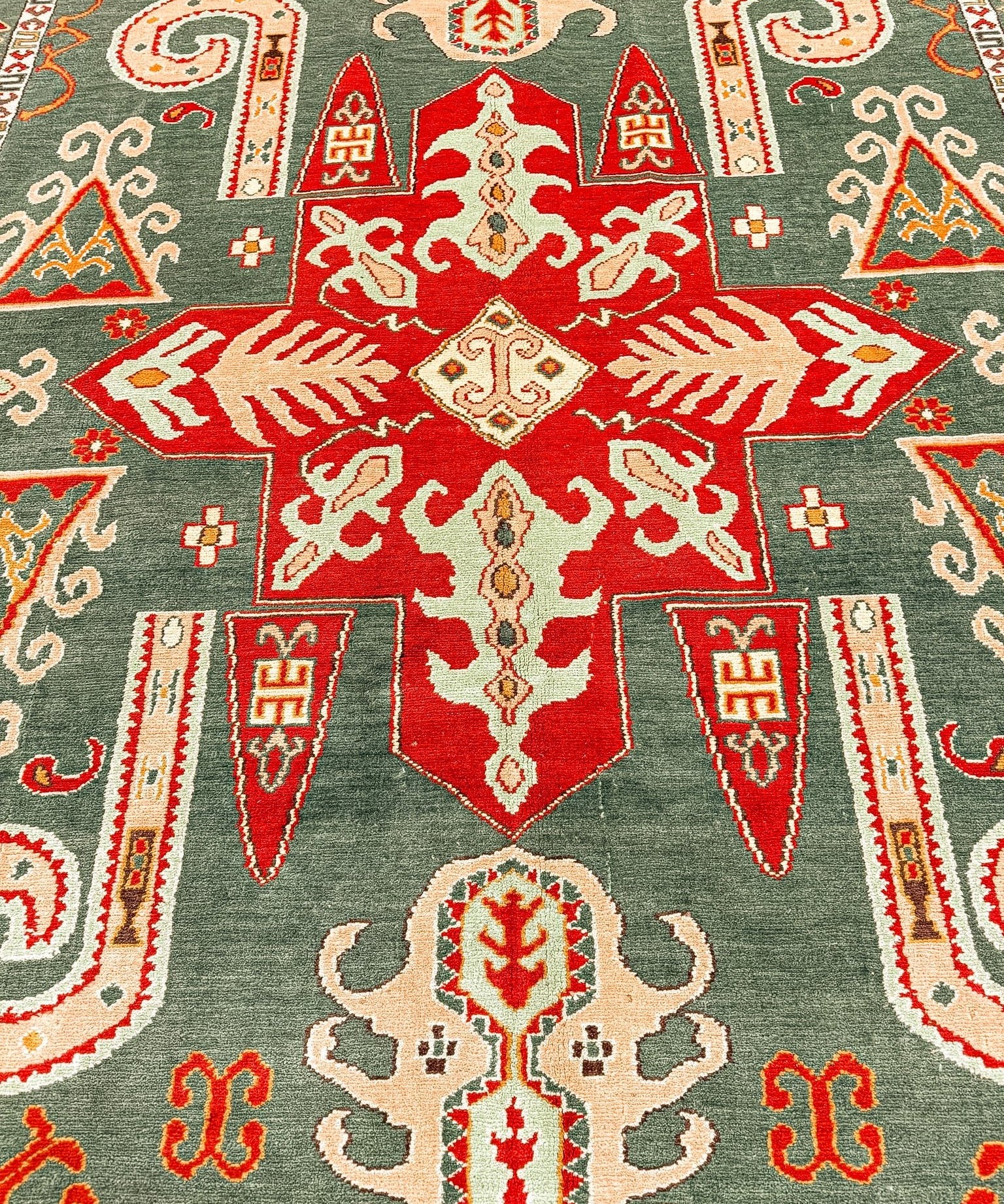 Kazak rug close-up with red central motif on dark green, surrounded by cream scrollwork.