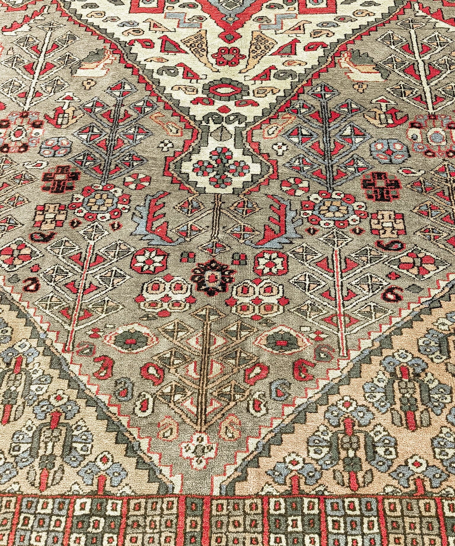 Egyptian oriental rug top view, cream and gray field with red diamond motifs and blue accents