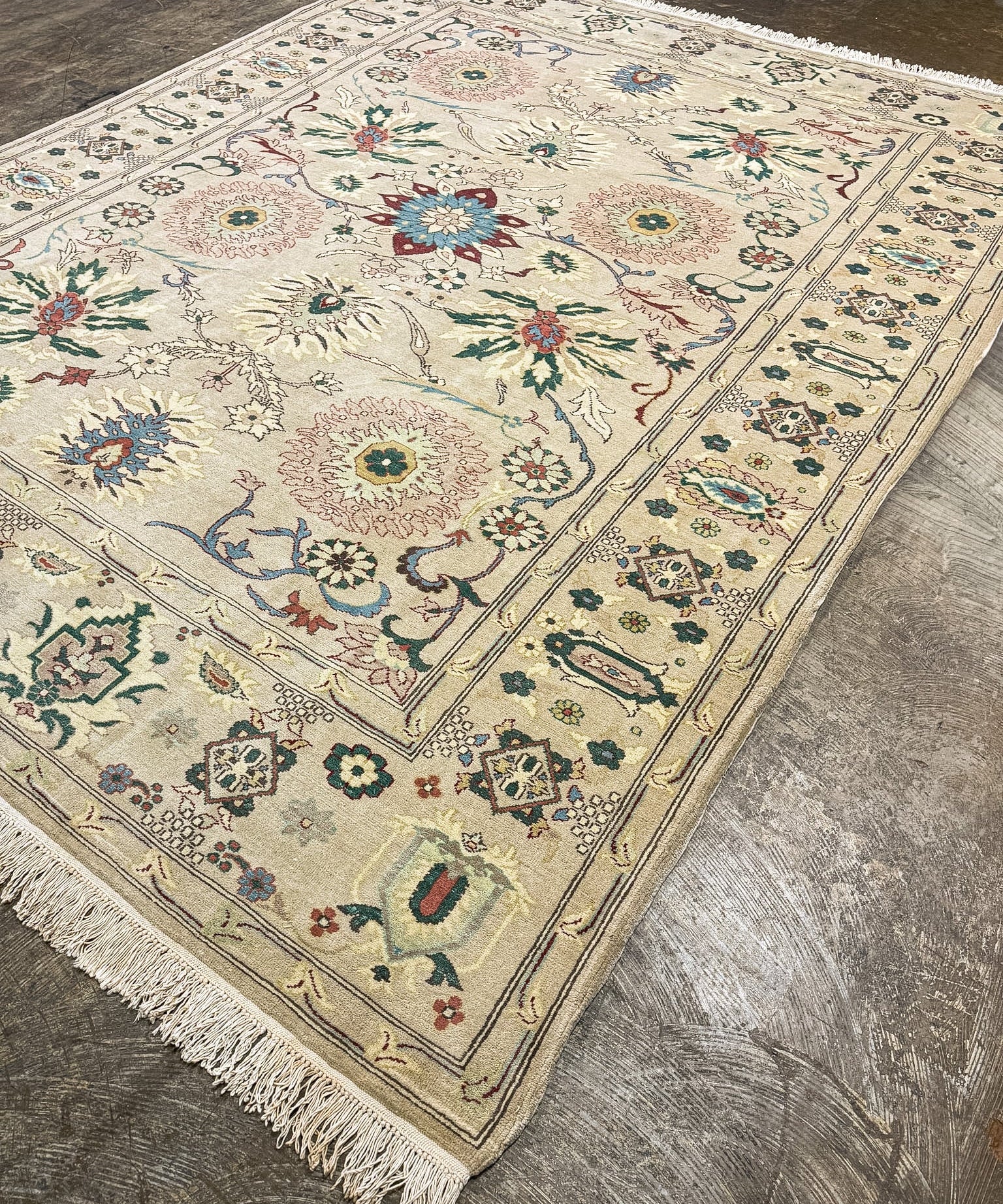 Ivory Sultanabad rug shown at angle with floral rosette medallions, multicolor border, and fringe.
