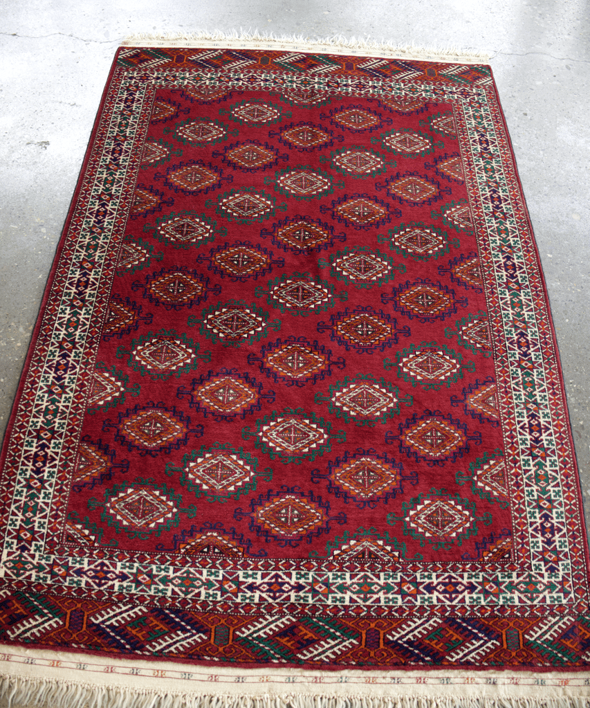 Red Bukhara-style area rug with central pattern and detailed multicolor border; fringed edge.