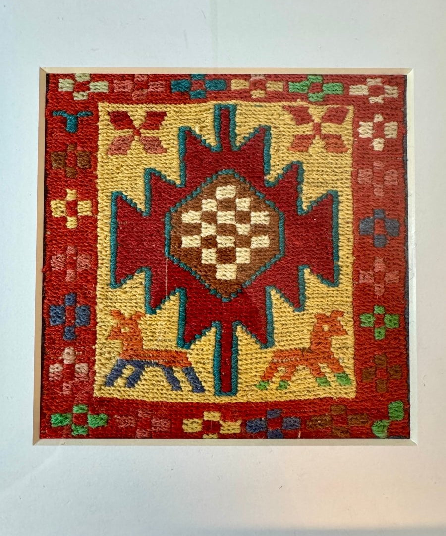Framed kilim rug with red border and central star medallion in yellow, blue, and green.
