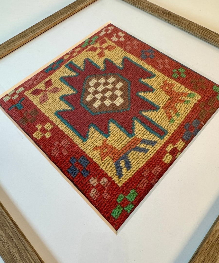 Framed kilim rug close-up with red and cream geometric diamond center; blue and green accents.
