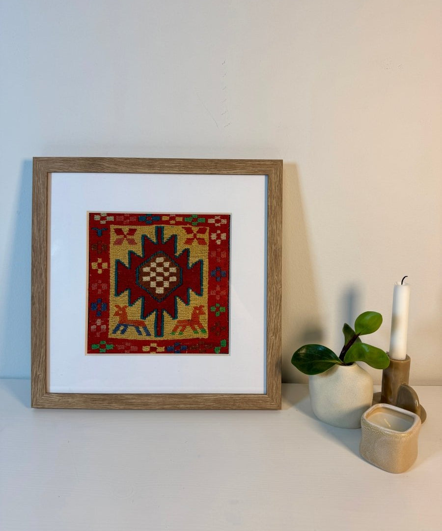 Framed square kilim rug with red field and geometric stars; border in green, blue, yellow.