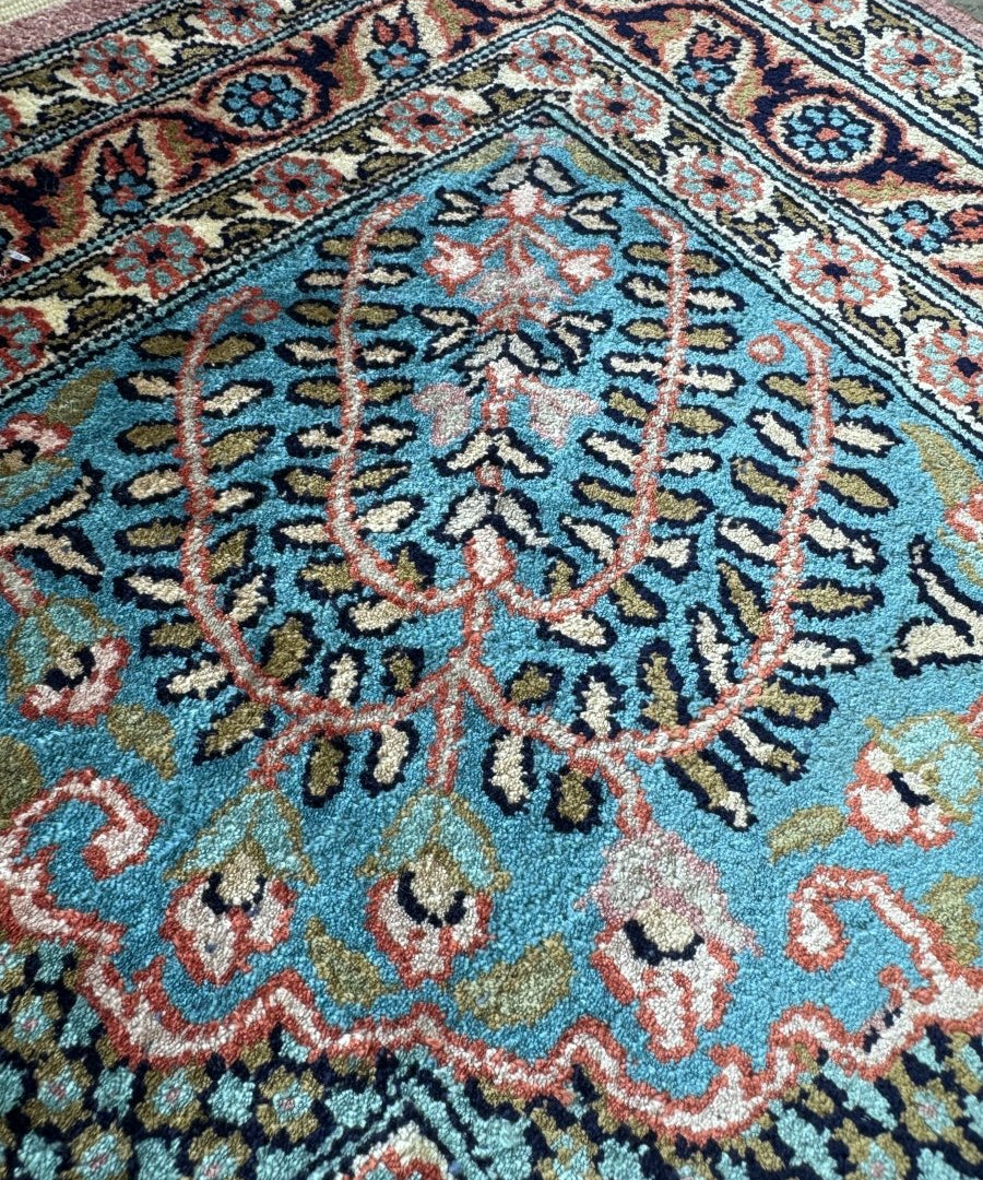Close-up of blue rug corner with ornate floral center and multicolor lattice details.
