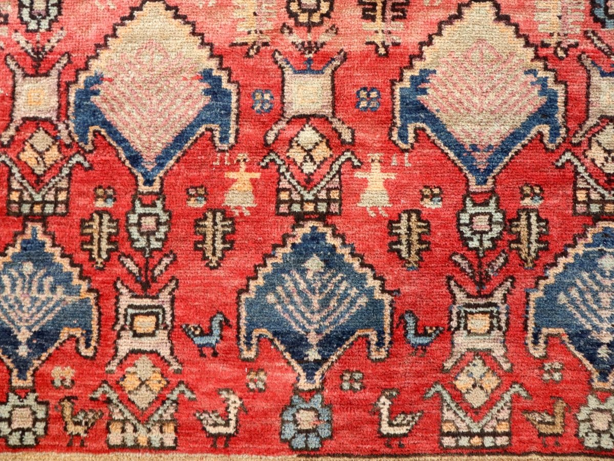 Close-up of red rug with repeating cream-and-navy diamonds and corner motif lines