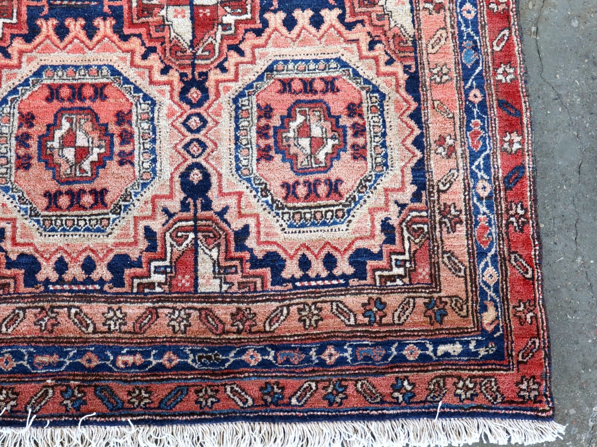 Persian runner rug corner with red and navy medallions and short fringe edge