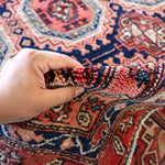 Persian runner rug edge with hand gripping short fringe; red navy and cream pattern